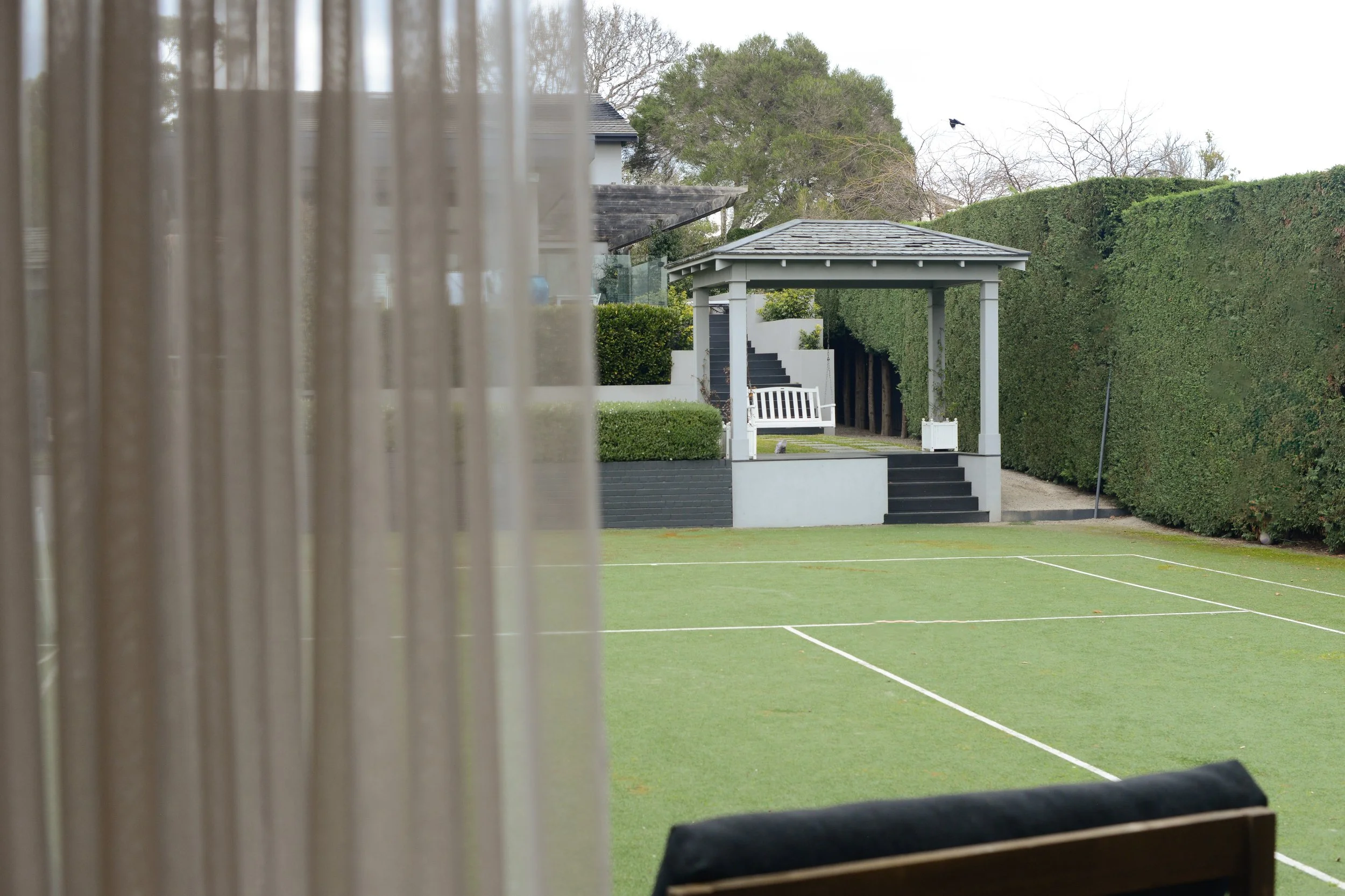 View from Driftwood Studio Mt Eliza with a covered seating area and trees in the background, seen from behind a sheer curtain.