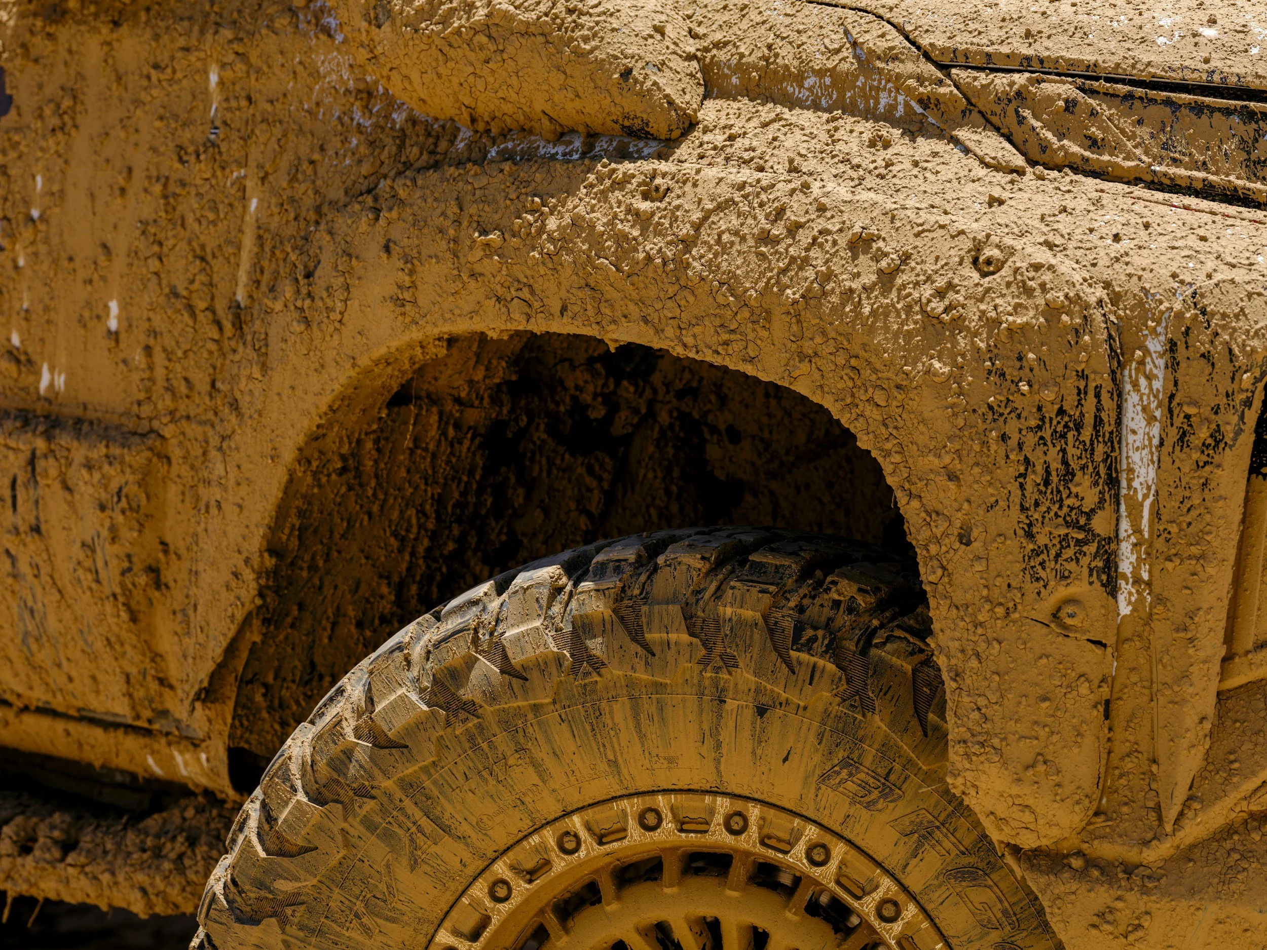 Close-up of a yellow construction vehicle, covered in dried mud, showing part of the wheel and its surrounding metal structure.
