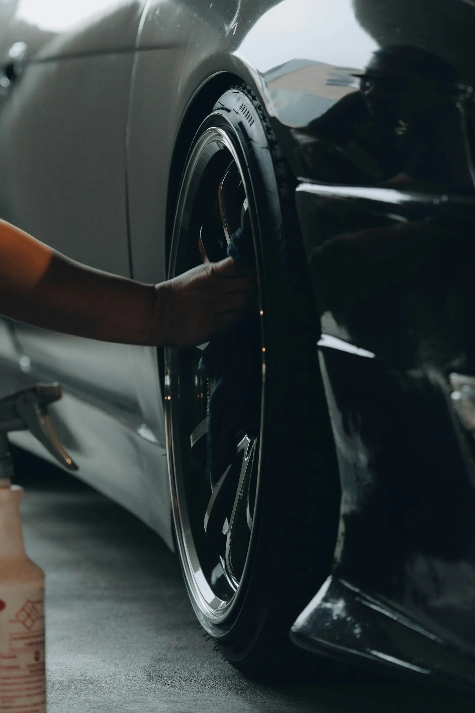 A person polishing the wheel of a sleek, black car in a garage.