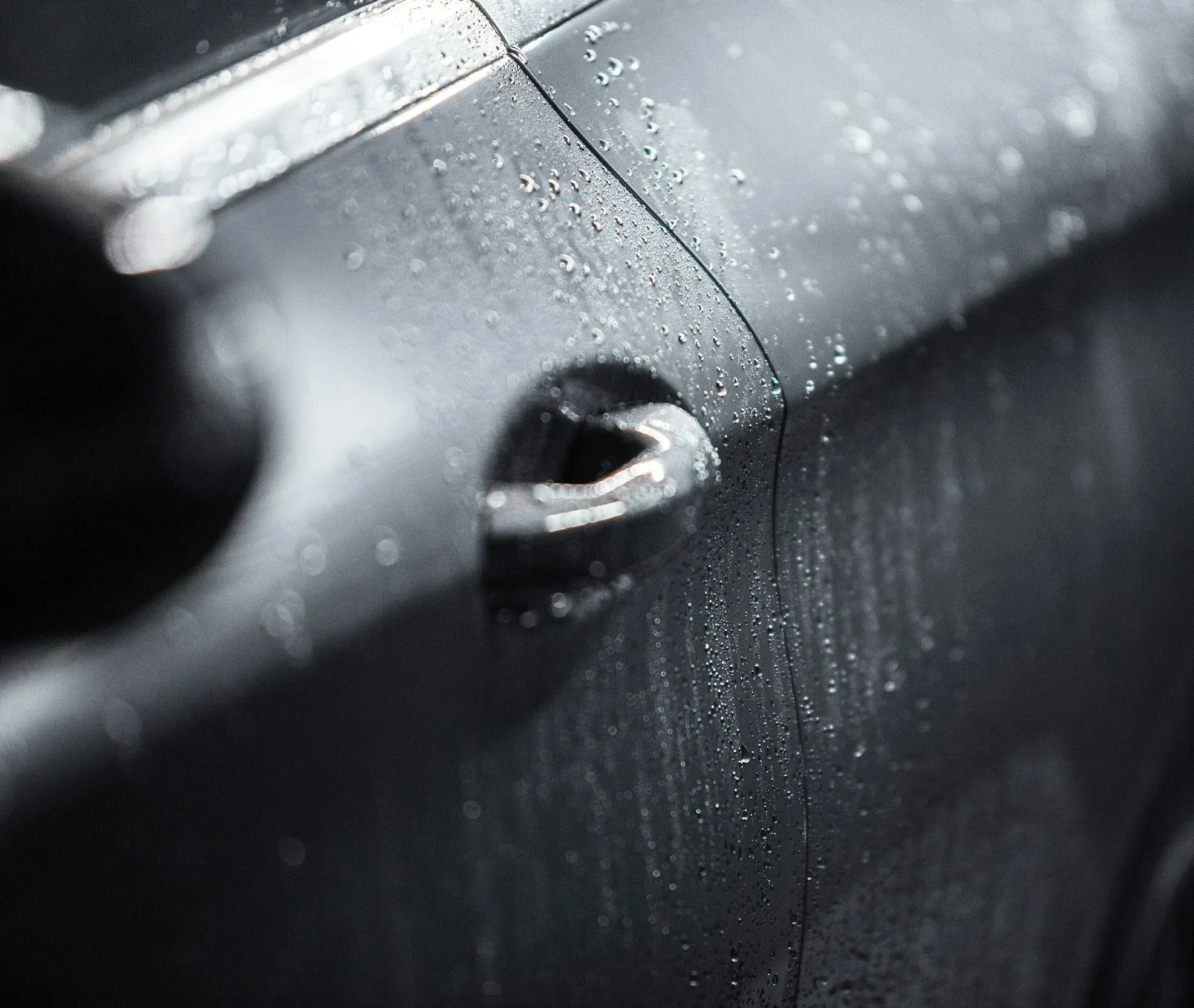 Close-up of a black car door with beading water droplets on its surface.