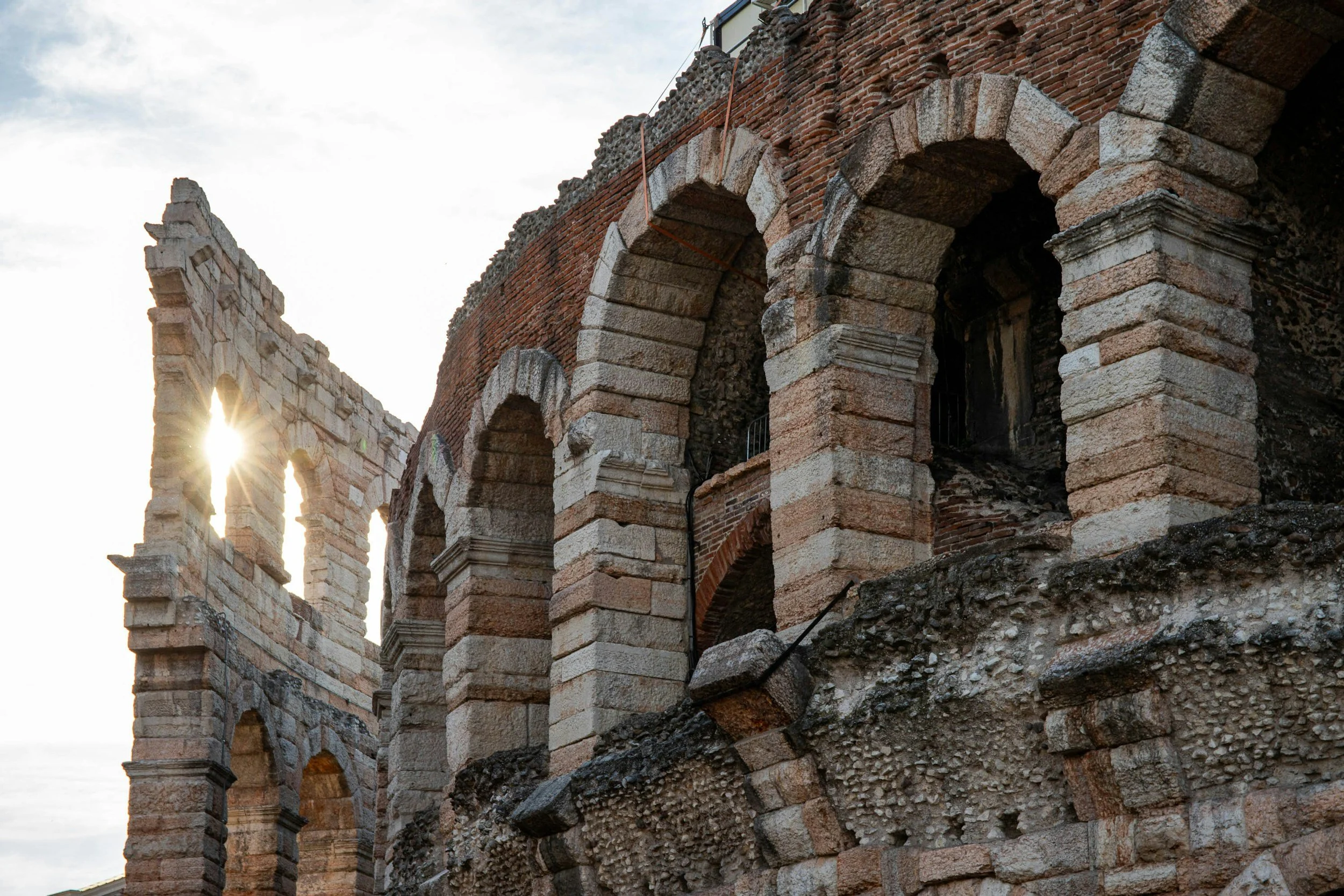Historic stone and brick ruins of an ancient Roman amphitheater with arches, captured at sunset.