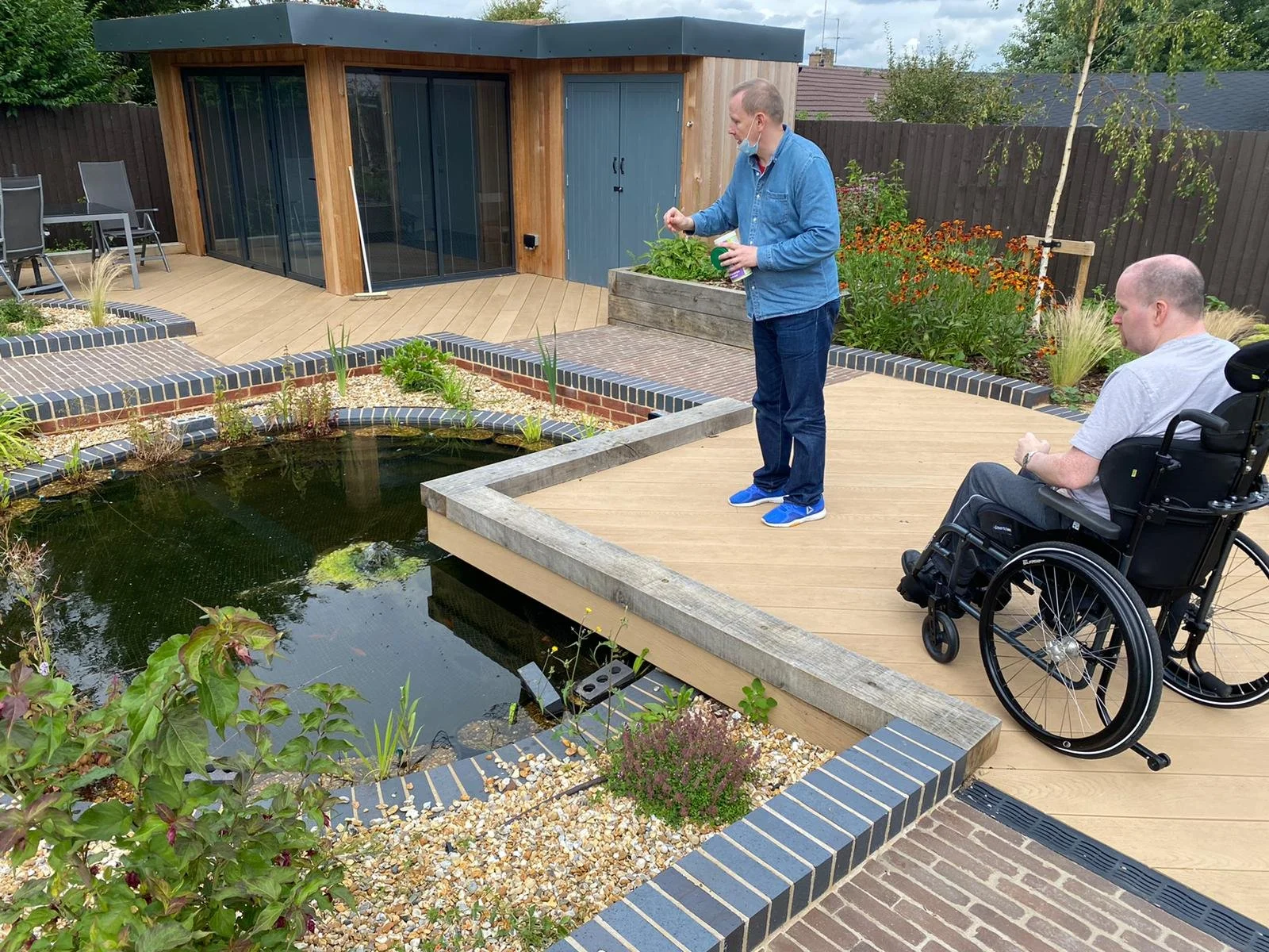 Two children in safety helmets and harnesses standing on crates in a warehouse, holding onto a climbing rope, smiling at the camera.