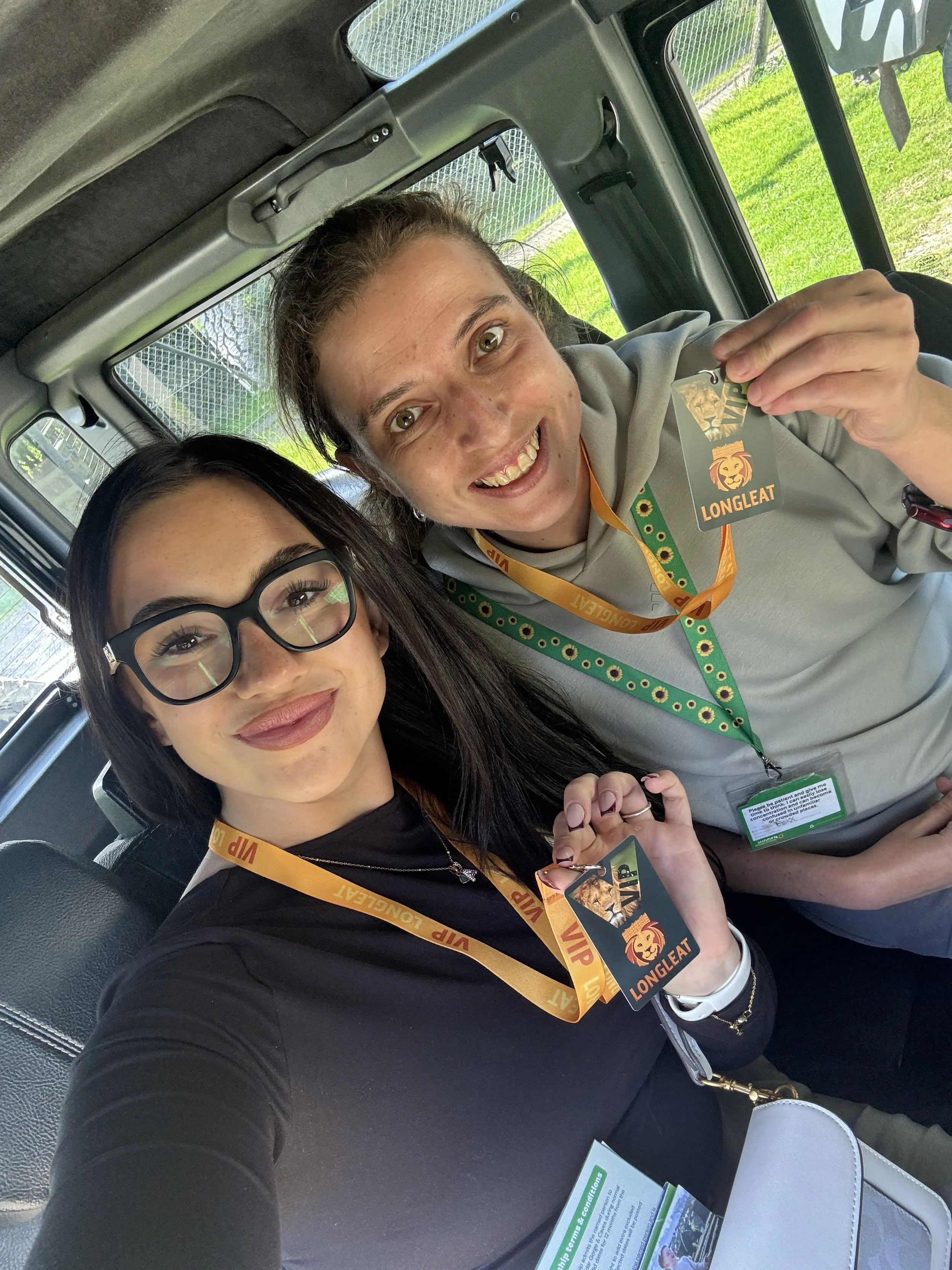 Two women sitting inside a vehicle, smiling and holding VIP badges with the Longleat lion logo, indicating they are visitors at Longleat.