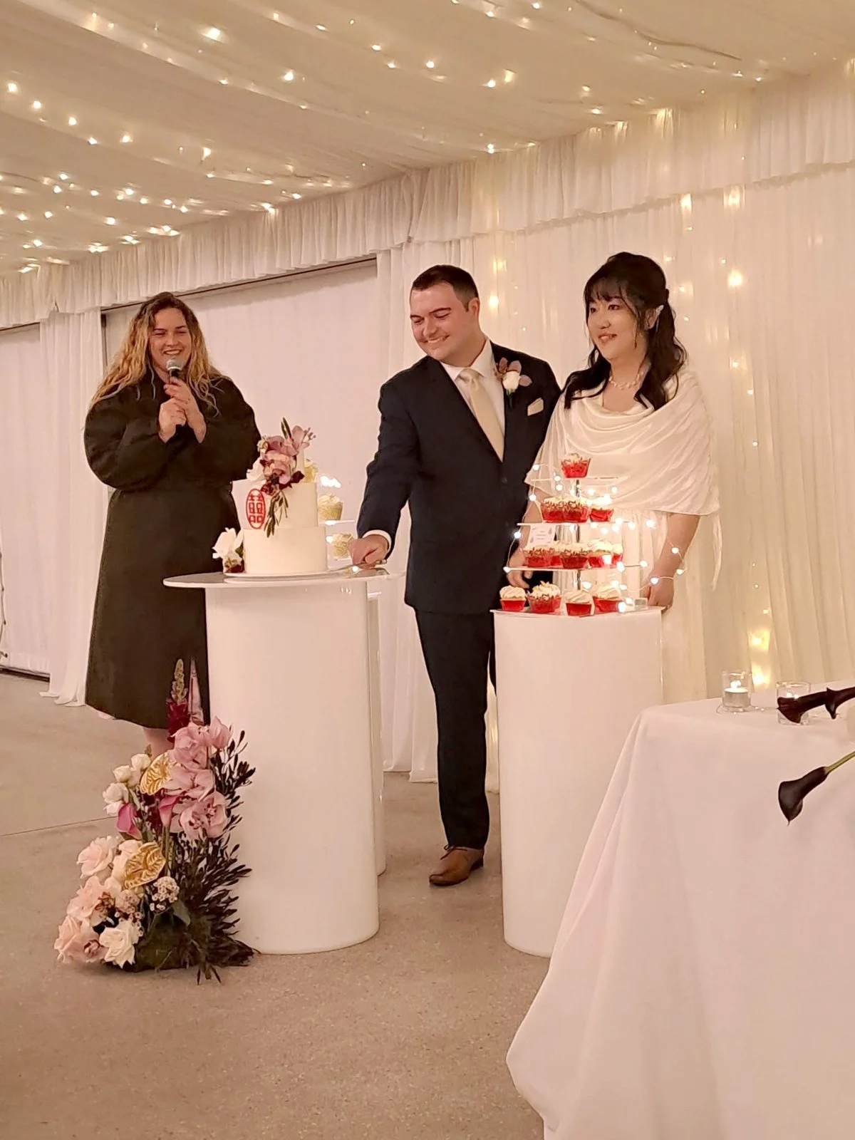Maddie Hayes MC-ing a wedding reception with a microphone as the bride and groom cut their cake