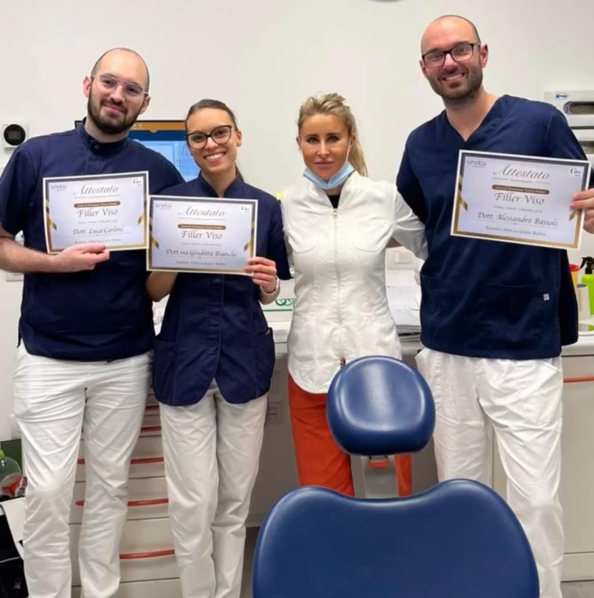 Gruppo di cinque professionisti in un ufficio medico, alcuni con certificati di riconoscimento, alcuni vestiti in divisa medica, sorridenti e felici.