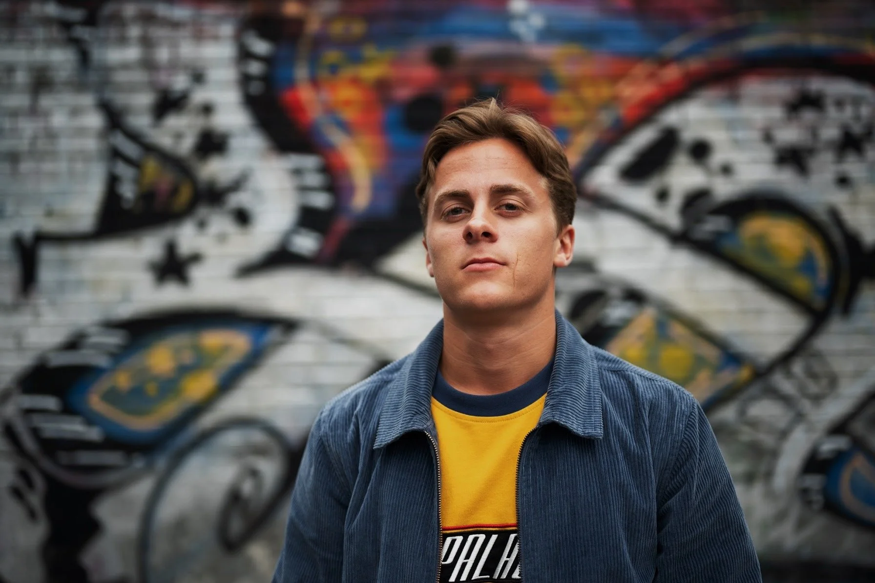 Ung mann står foran en vegg med graffiti.