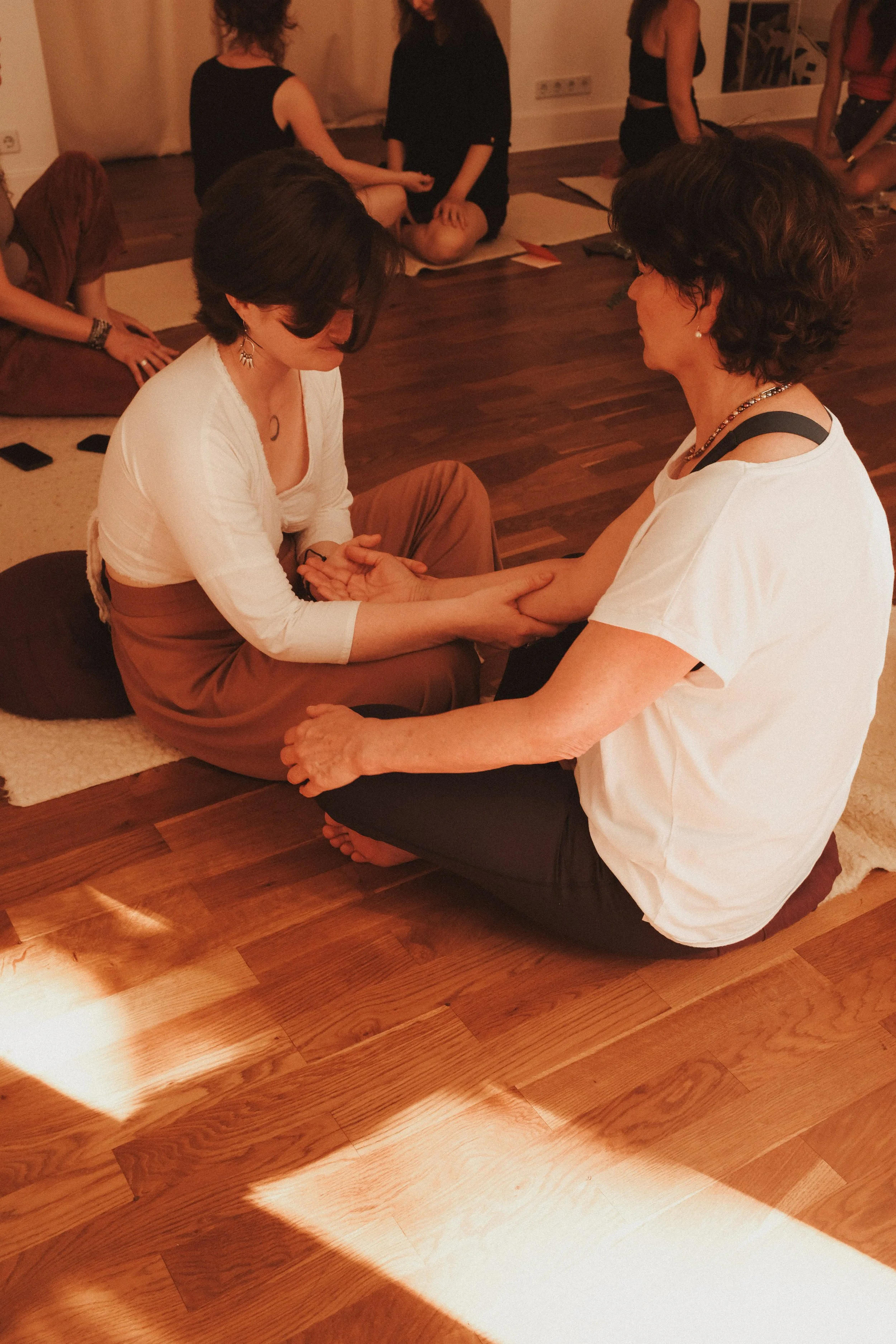 Zwei Frauen sitzen auf dem Boden, eine hält die Hand der anderen während einer Massage oder Heilbehandlung.