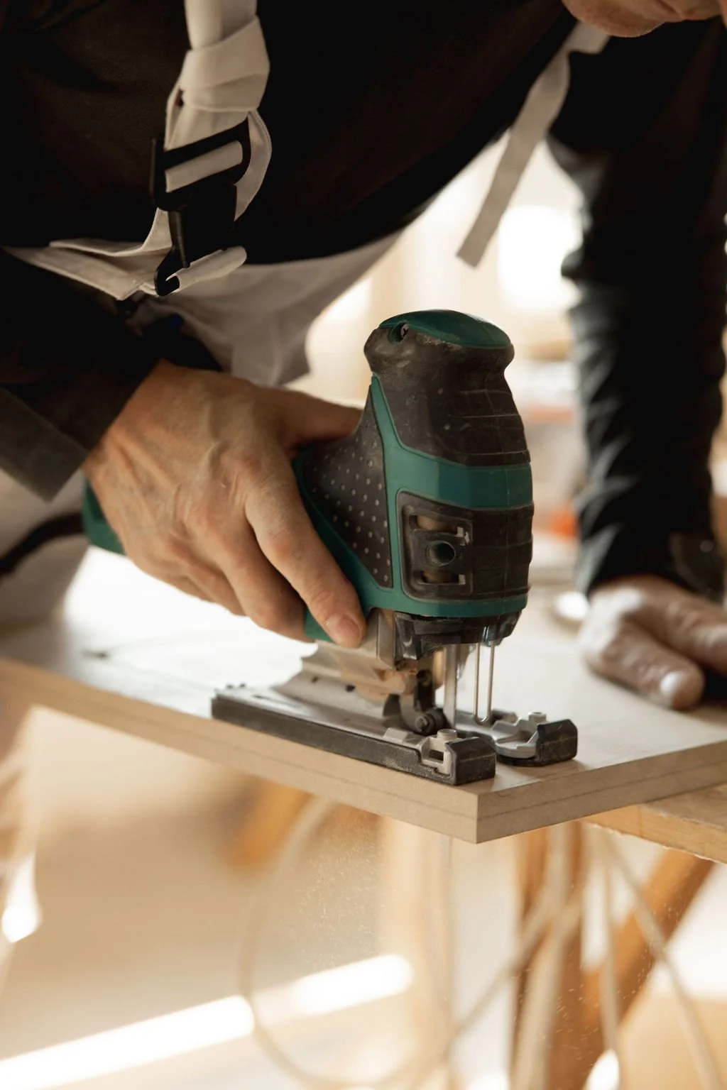 A craftsman carefully cuts a wooden board with a jigsaw in a workshop.