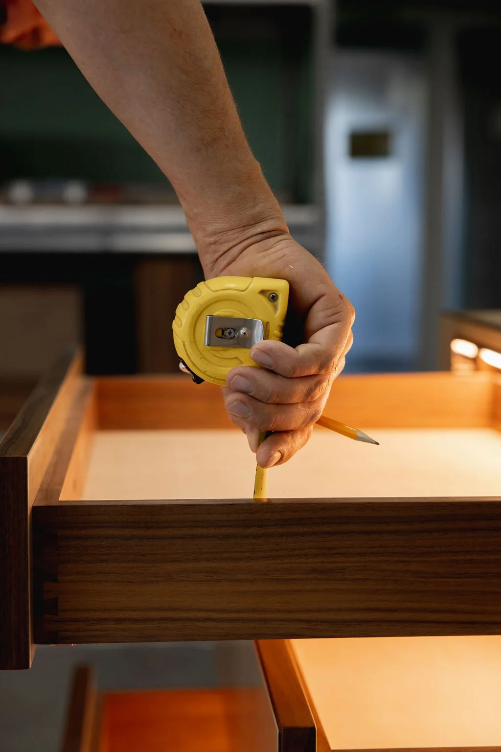A tape measure is used to check the inside dimensions of a wooden drawer, with a pencil held nearby.