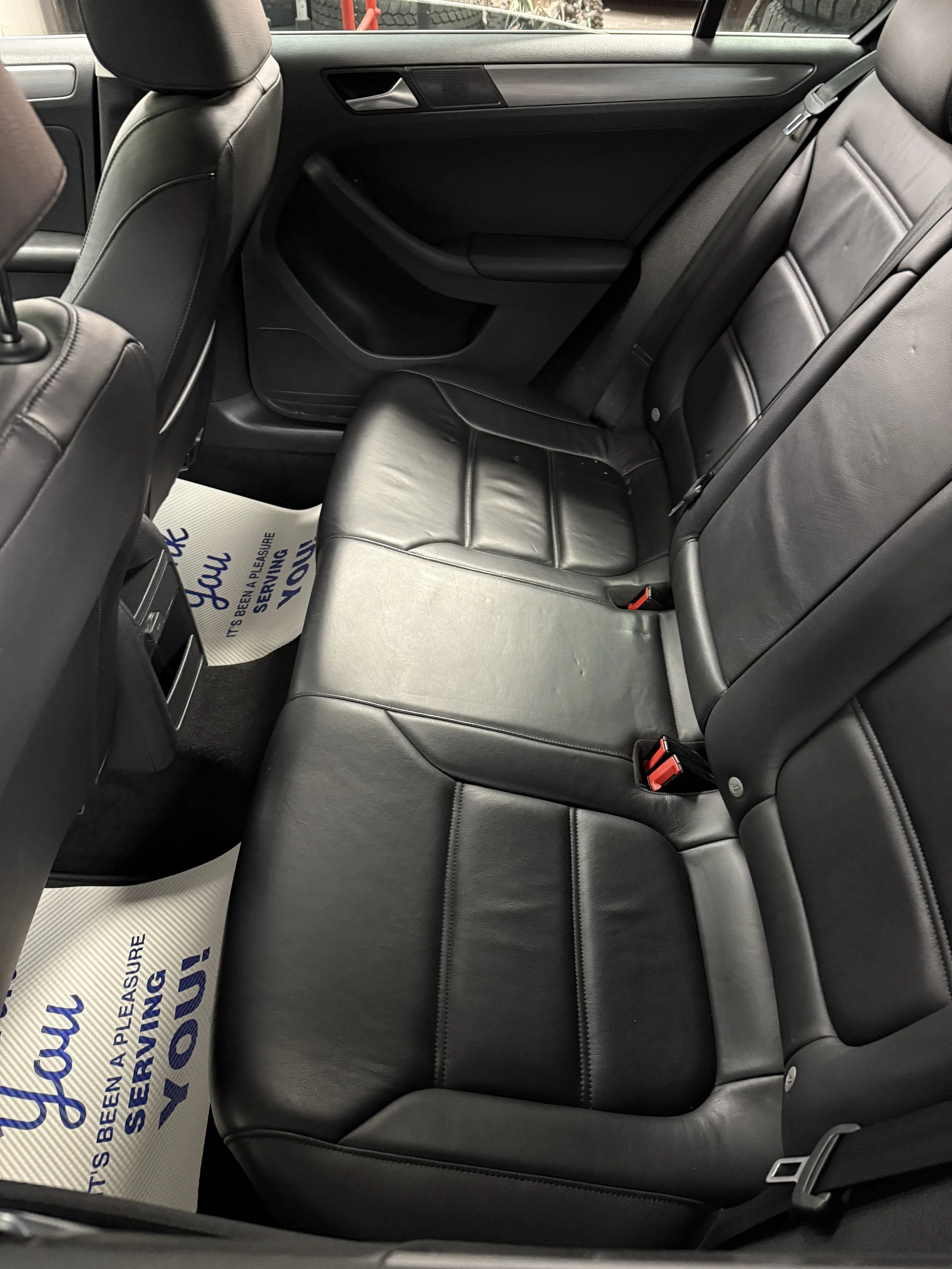 View of the backseat area of a car featuring black leather seats, black door panels, and floor mats with blue text.