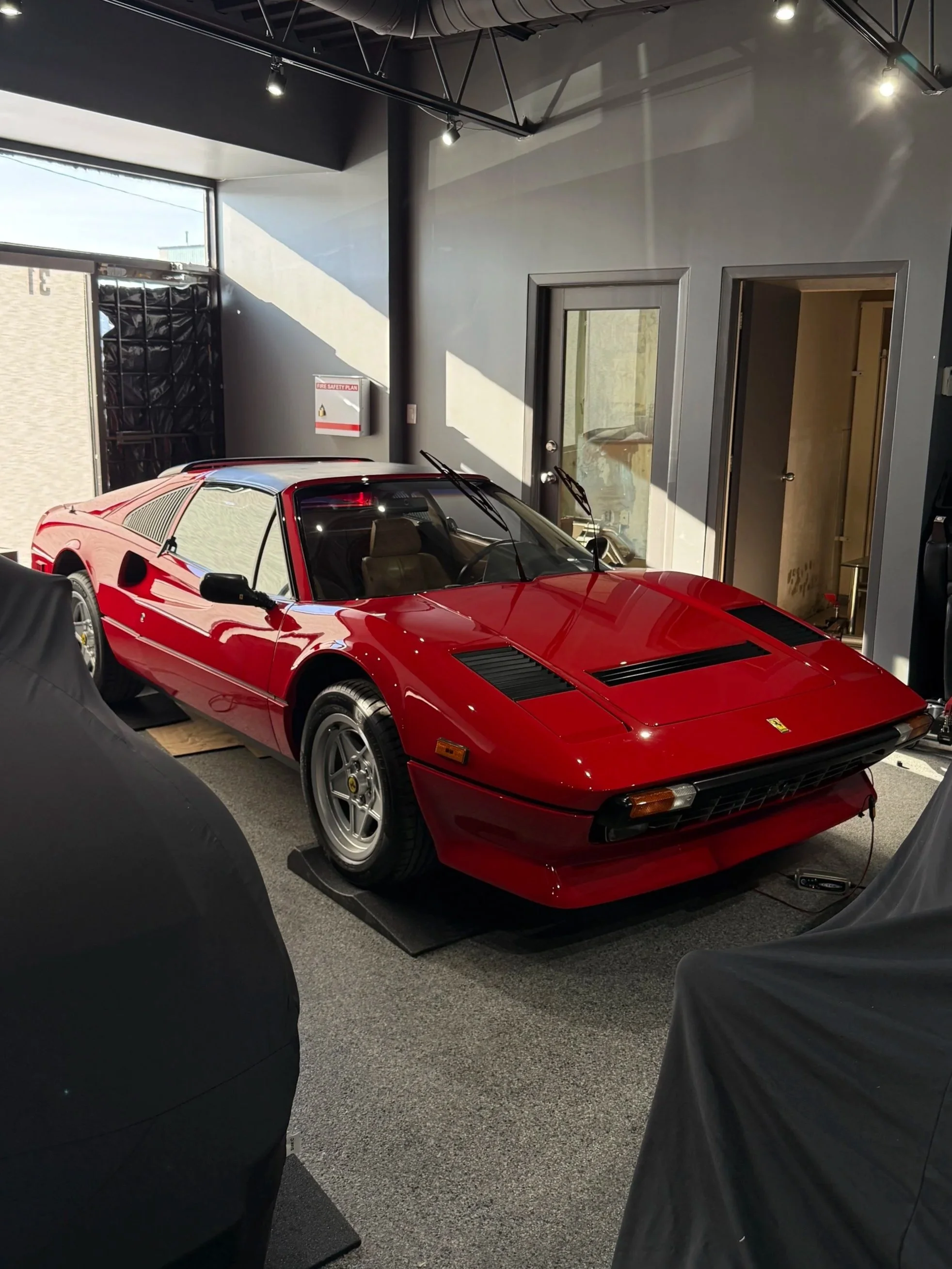 Red vintage Ferrari sports car parked indoors in a showroom with sunlight coming through the windows.