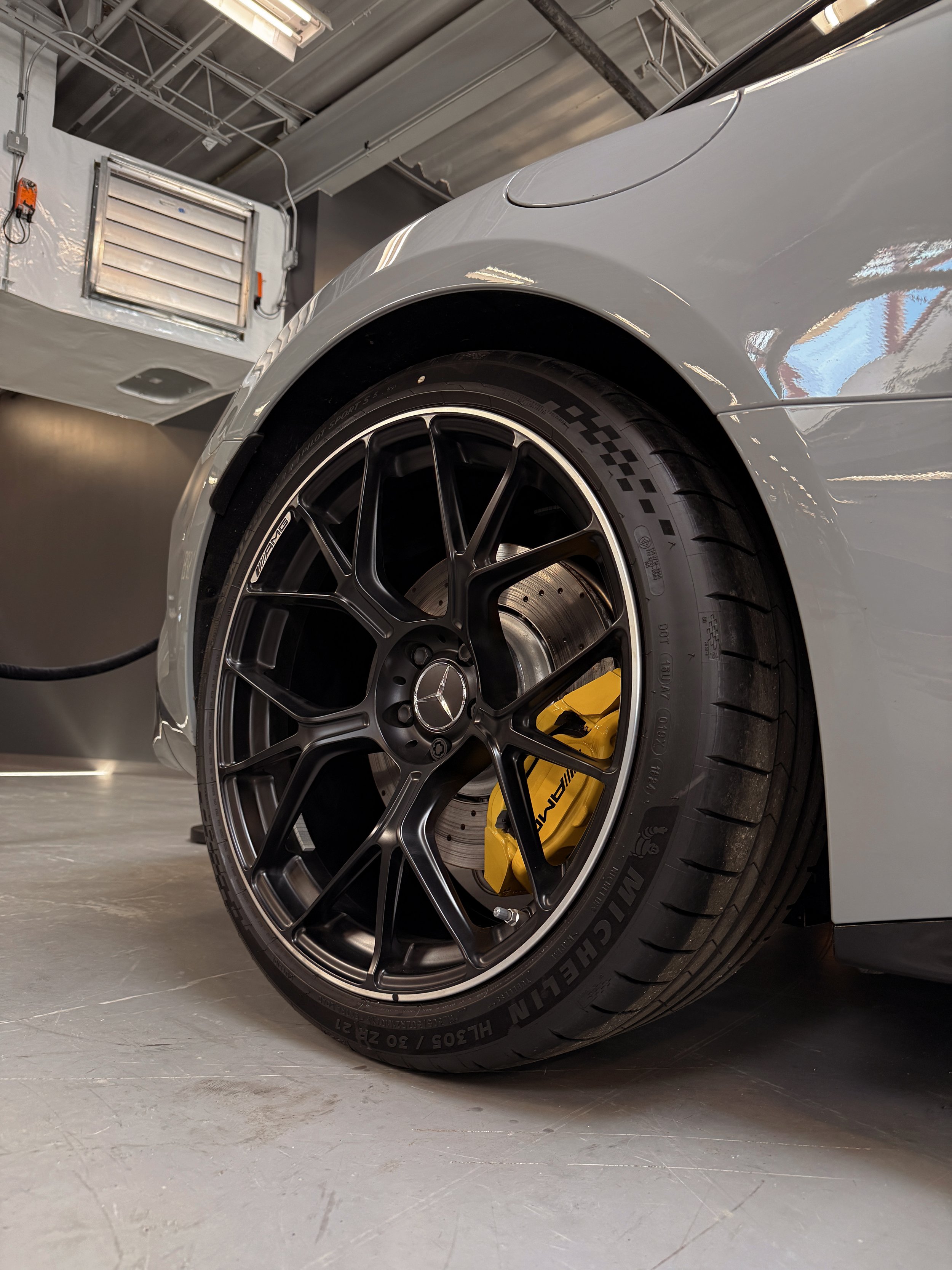 Close-up of a silver luxury car wheel with a black rim and yellow brake caliper, parked indoors on a concrete floor.