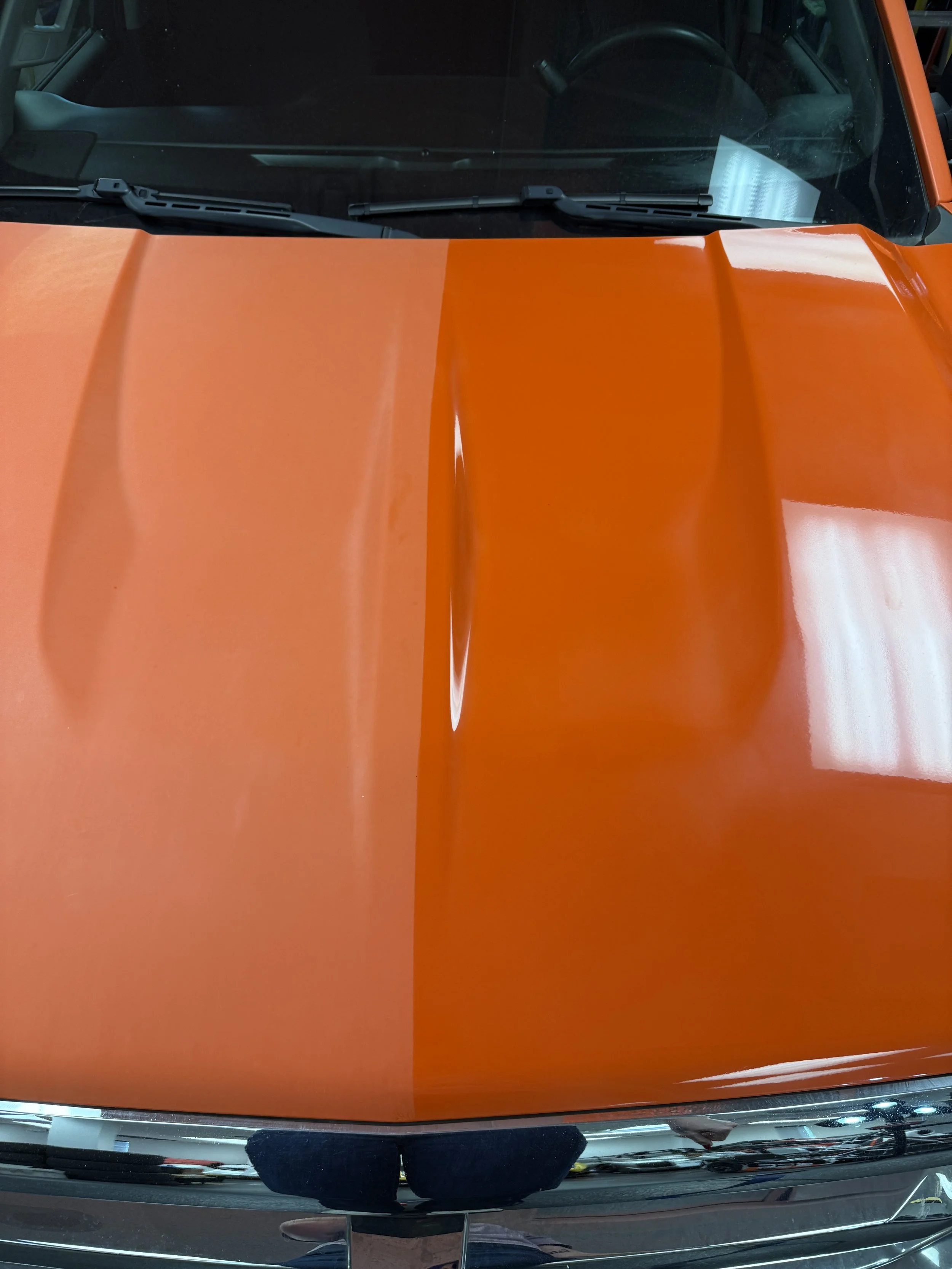 Close-up of a shiny orange car hood with a central raised section.