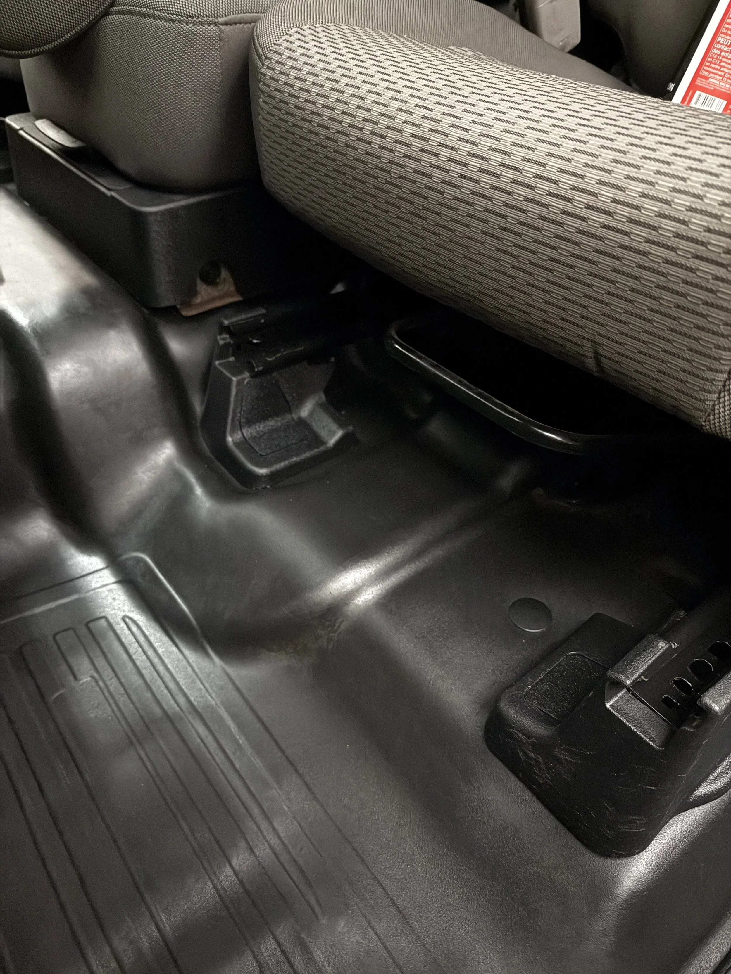 Interior of a vehicle showing the floor and seat mounting area, including a black metal mounting bracket and the underside of the seat.