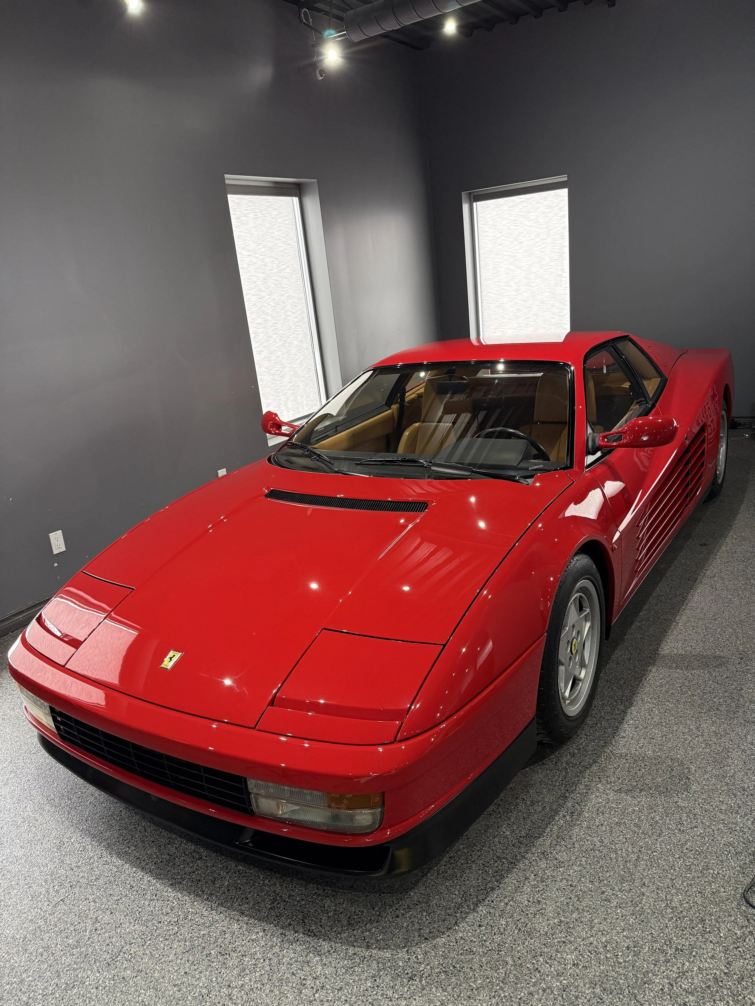 Red Ferrari sports car on display in a showroom with dark gray walls and two windows.