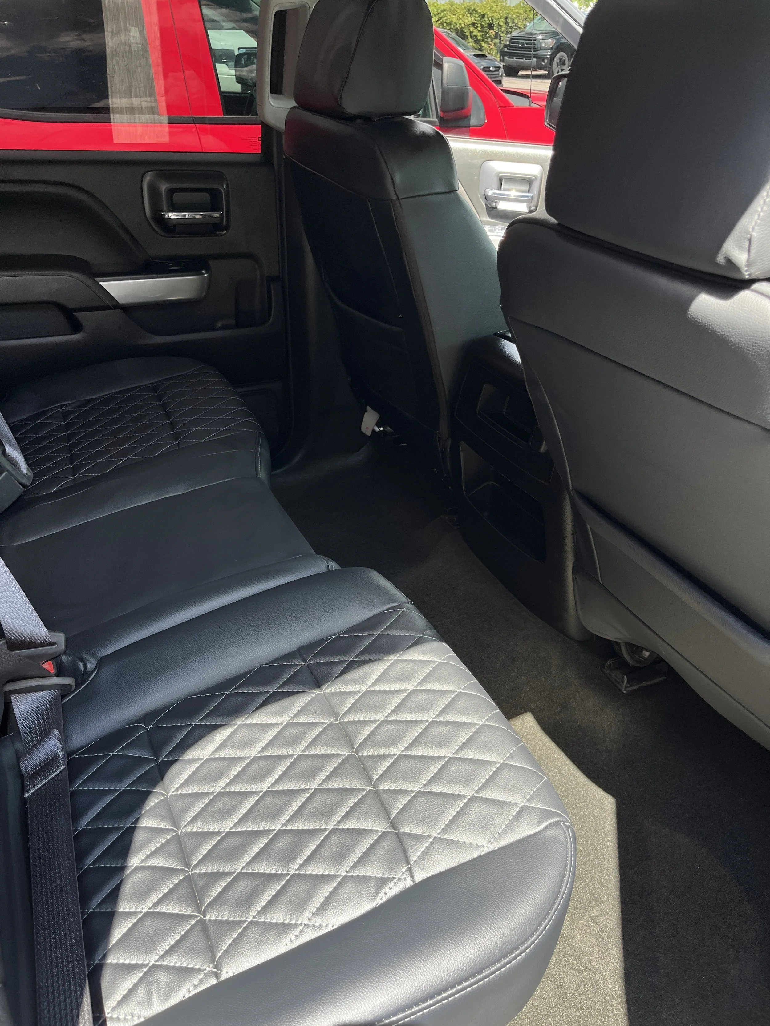 The backseat of a vehicle with black diamond-stitched leather seats and black interior, view of the rear passenger area with vehicles outdoors visible through the windows.