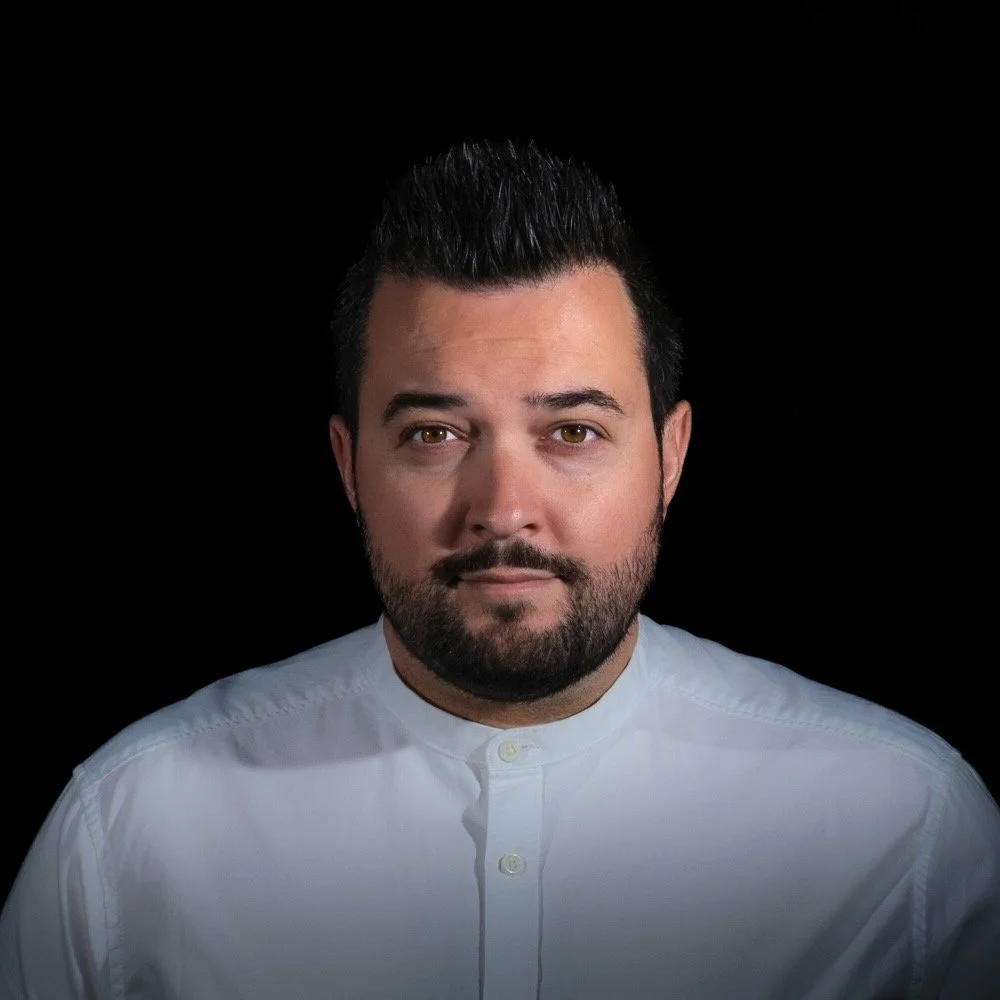 Portrait d'un homme avec une barbe portant une chemise blanche, fond noir.
