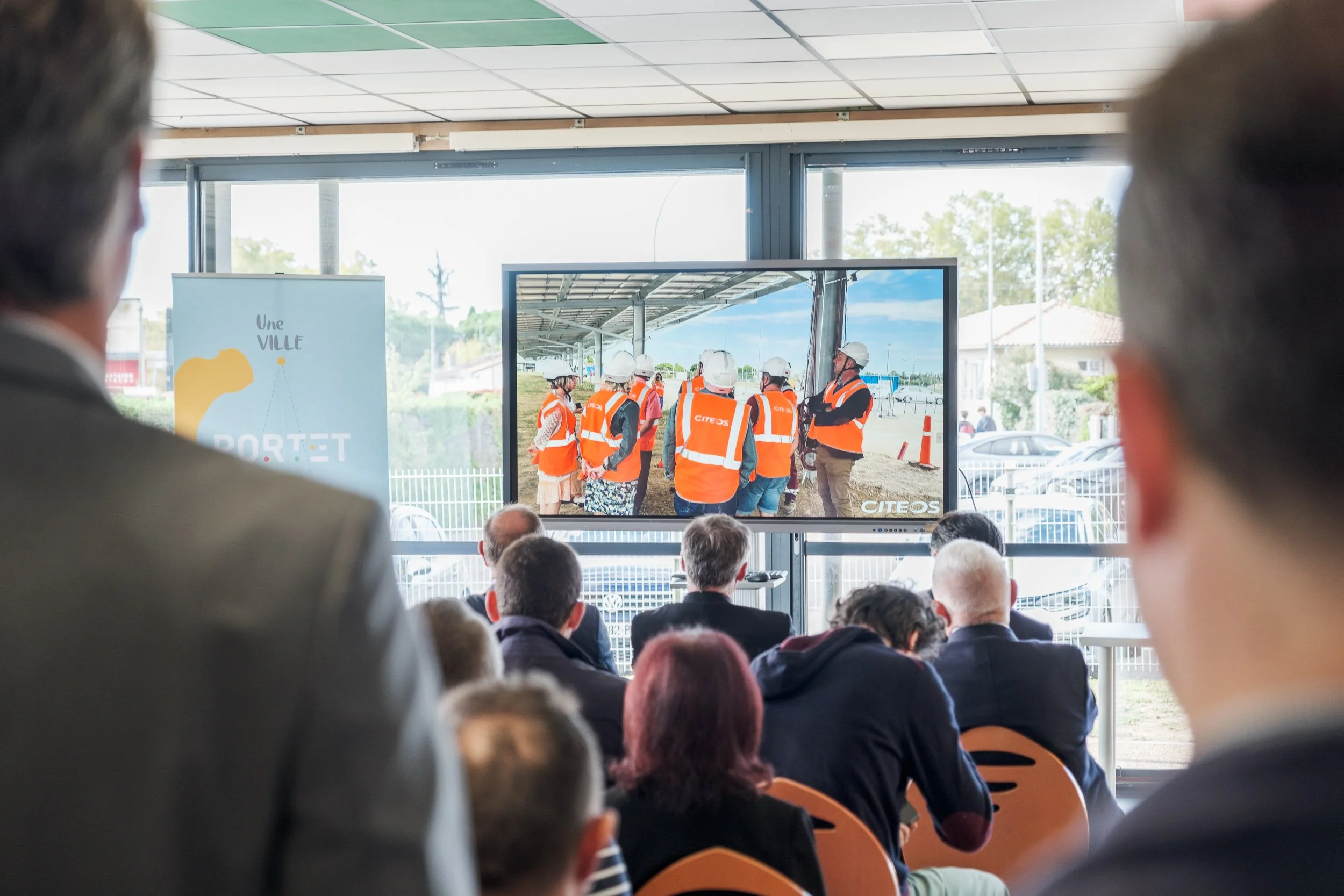 Présentation lors d'une conférence avec un écran montrant un groupe de personnes en gilets orange de chantier, sous un auvent.