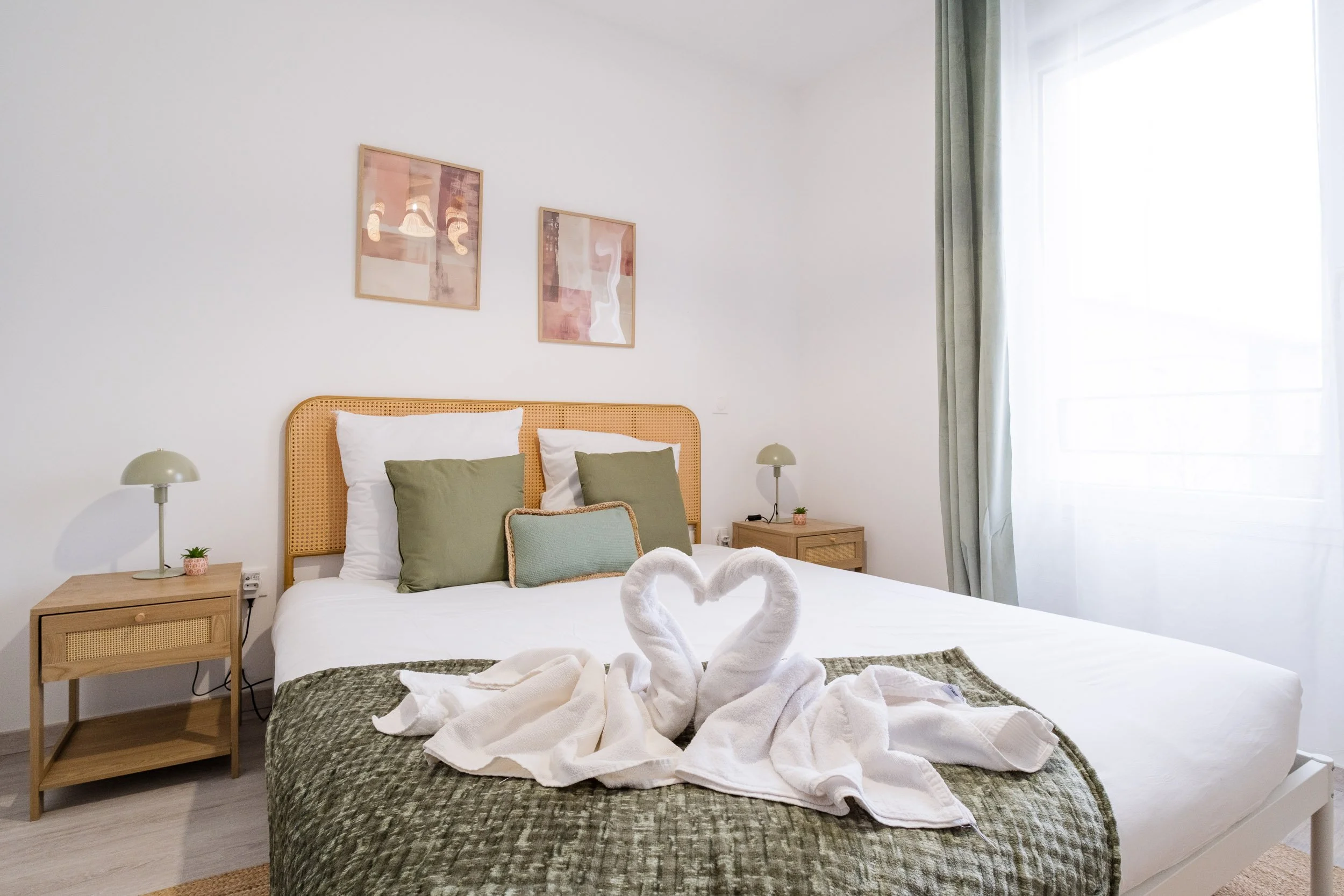 Chambre avec lit double, oreillers verts et blancs, décor minimaliste, deux lampes de nuit, deux tableaux abstraits, grande fenêtre avec rideaux.