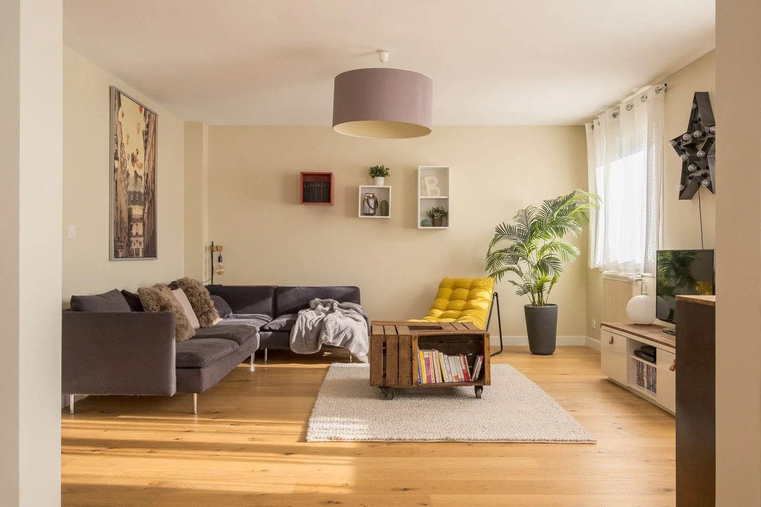 Salon moderne avec canapé gris, fauteuil jaune, plante verte, télévision, et décoration intérieure