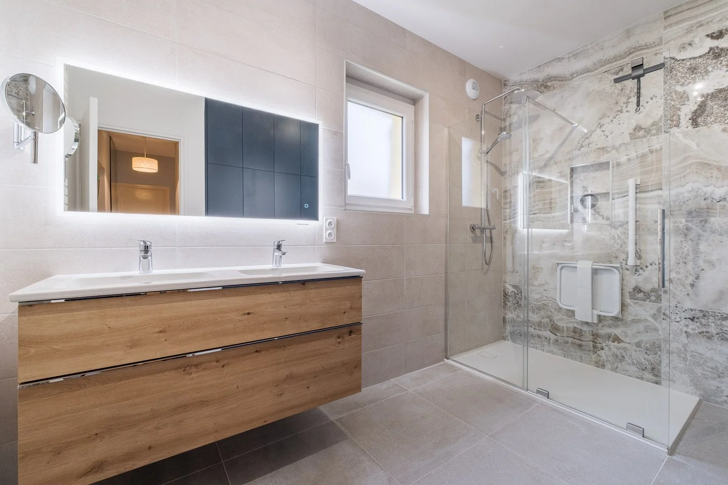 Salle de bain moderne avec double lavabo, miroir éclairé, vitre de douche, murs en pierre et fenêtre