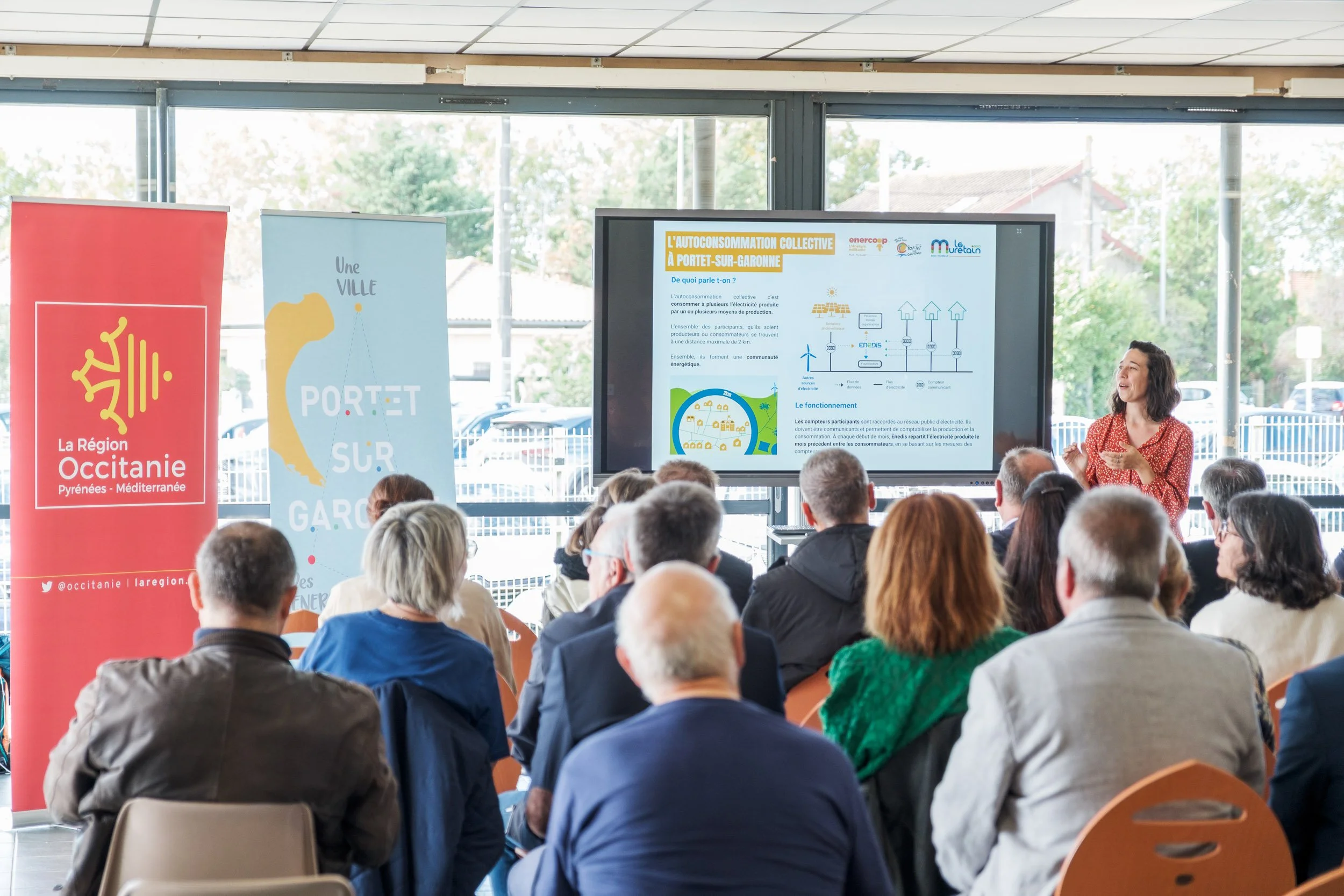 Une présentation dans une salle avec un écran affichant des informations sur la consommation collective d'énergie solaire, devant un groupe de personnes assises et écoutant.