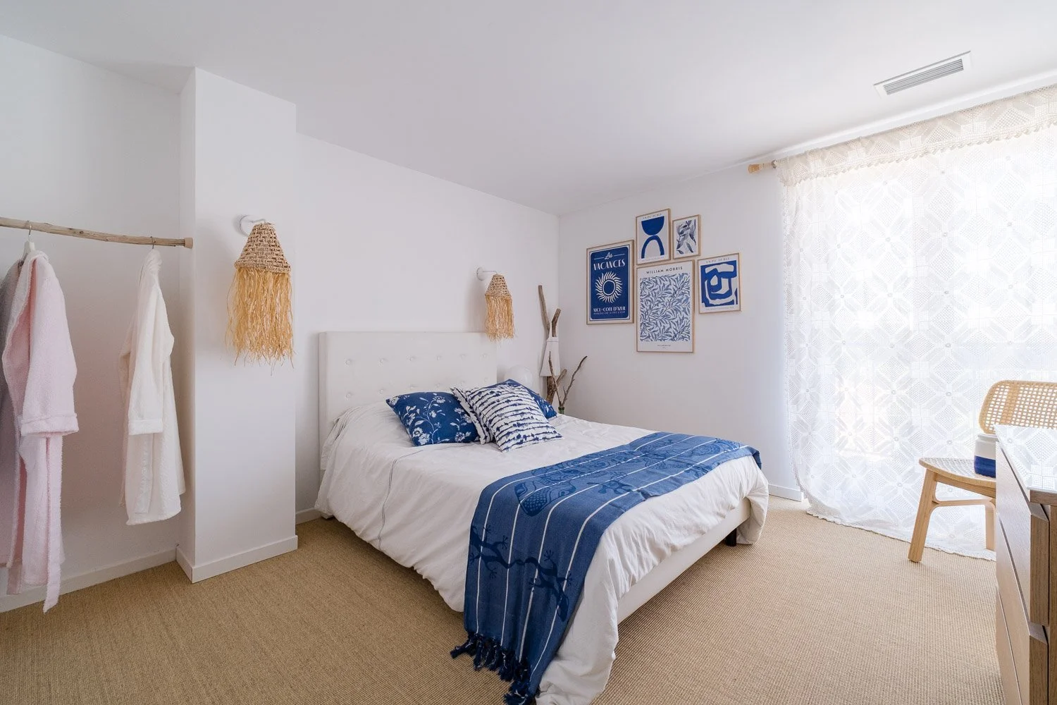 Chambre avec un lit blanc, oreillers bleus, décoration bleue, rideau en voile blanc, murs blancs, tapis beige, décor mural avec images bleues