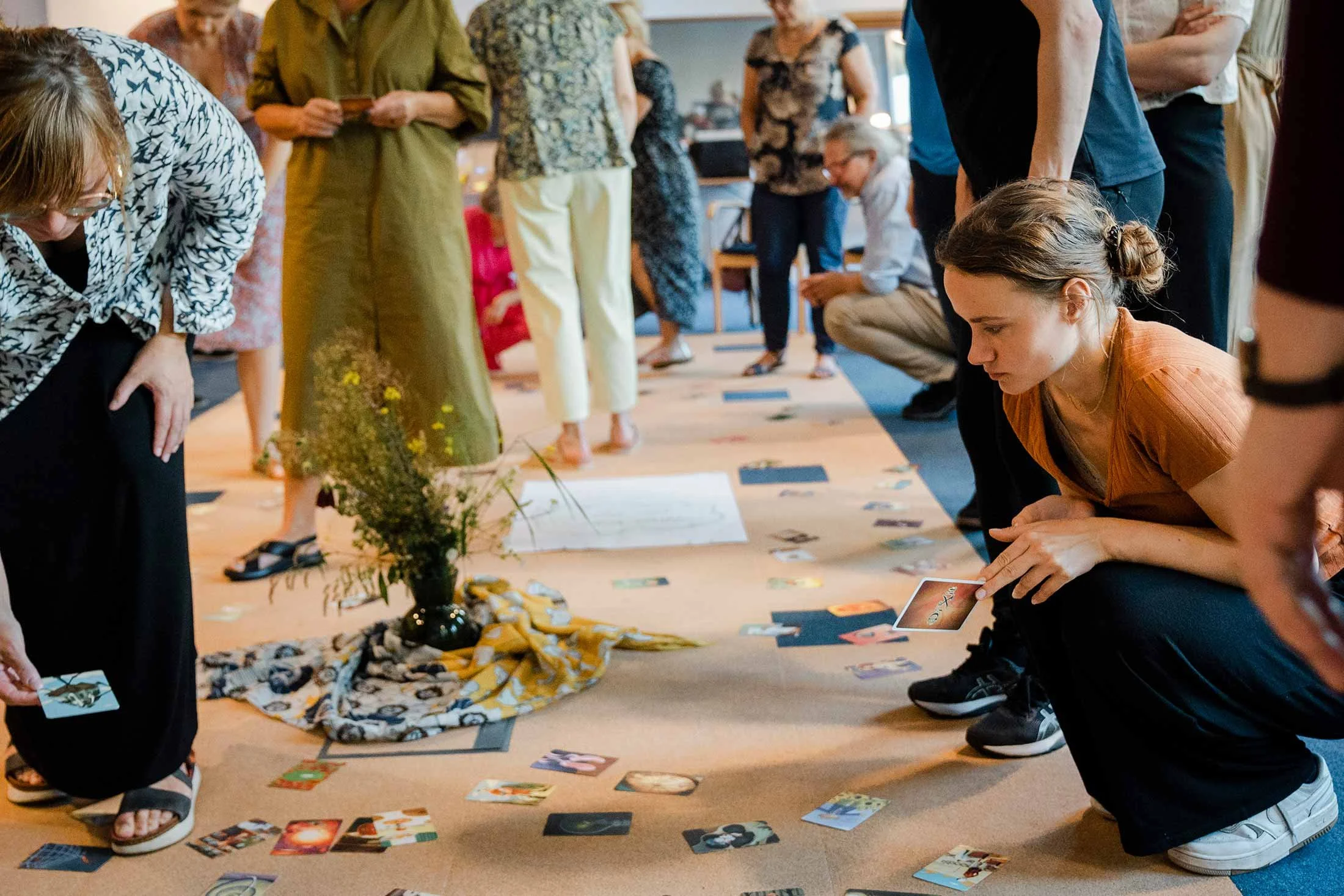 Group of people gathered around a table playing a card game in a room with a carpeted floor.