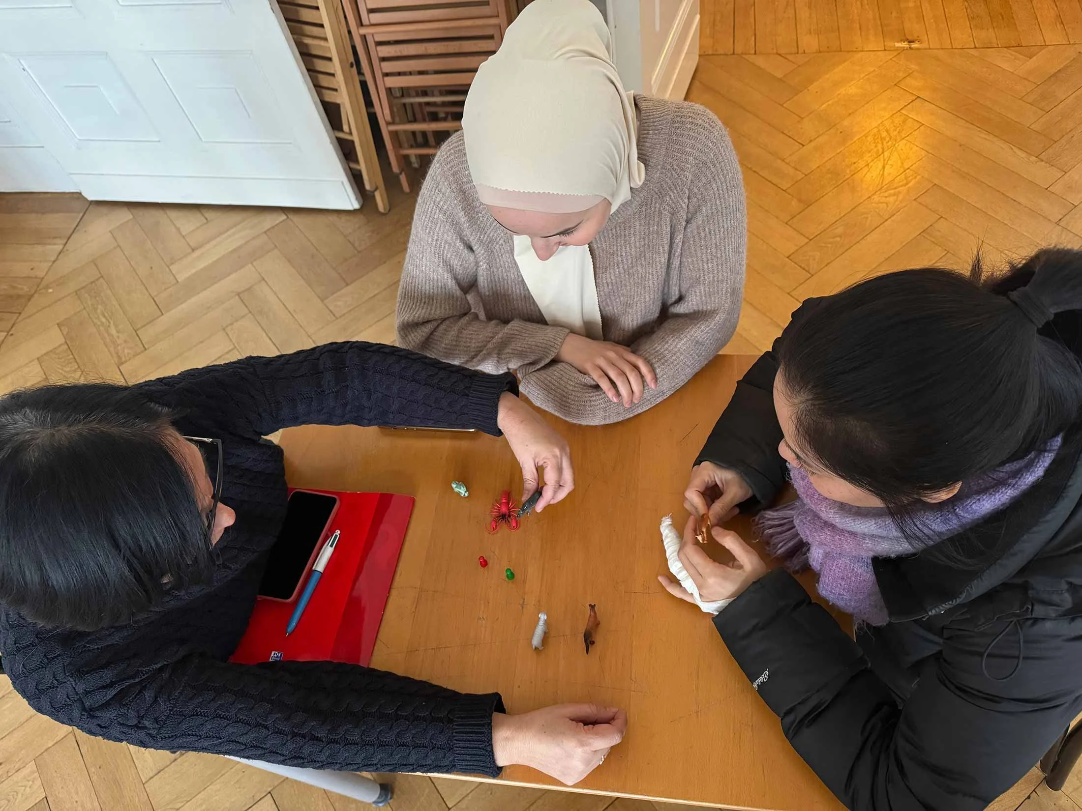 Four women sitting around a wooden table with Christmas-themed toys and decorations, engaging in conversation.