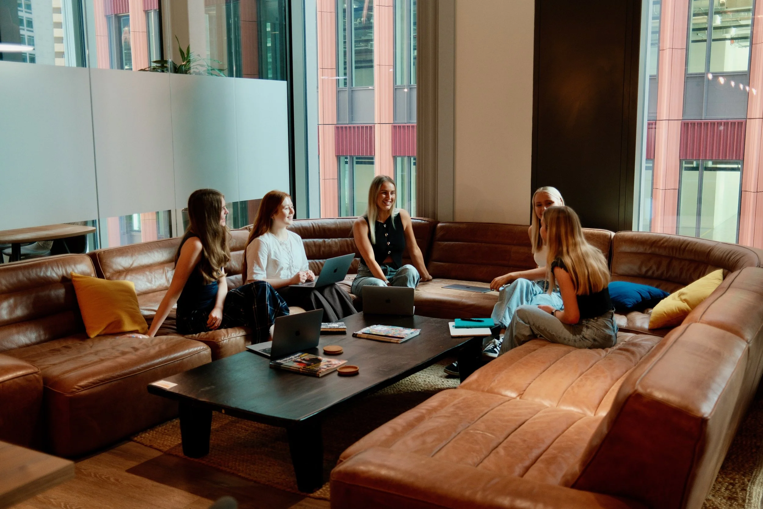 Team in large leather sofa meeting space – "Informal brainstorming session at The Mind Collective, generating creative marketing ideas and brand strategies."