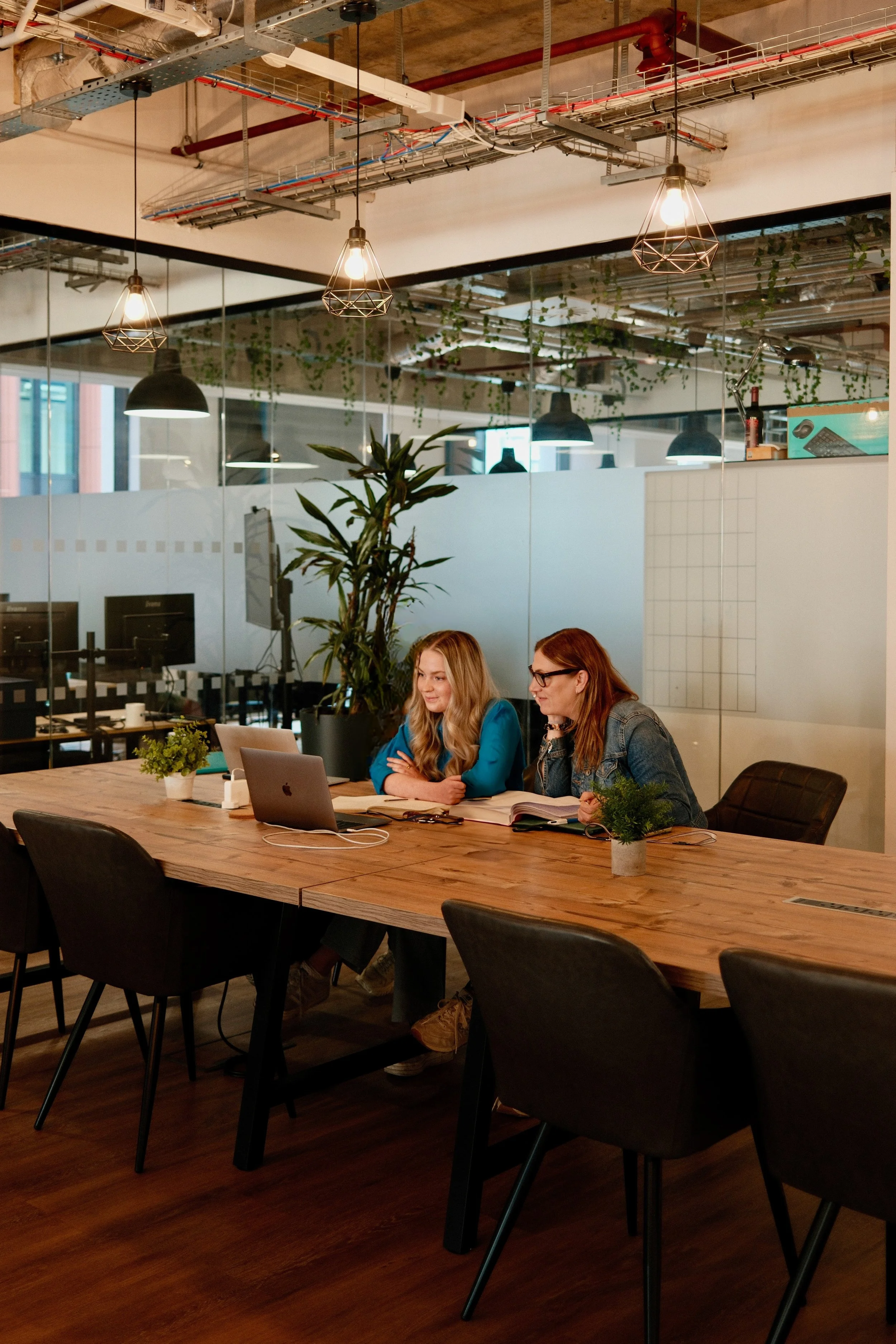 Two team members working on laptops at long table – "The Mind Collective strategists reviewing marketing campaigns and data-driven insights for clients."