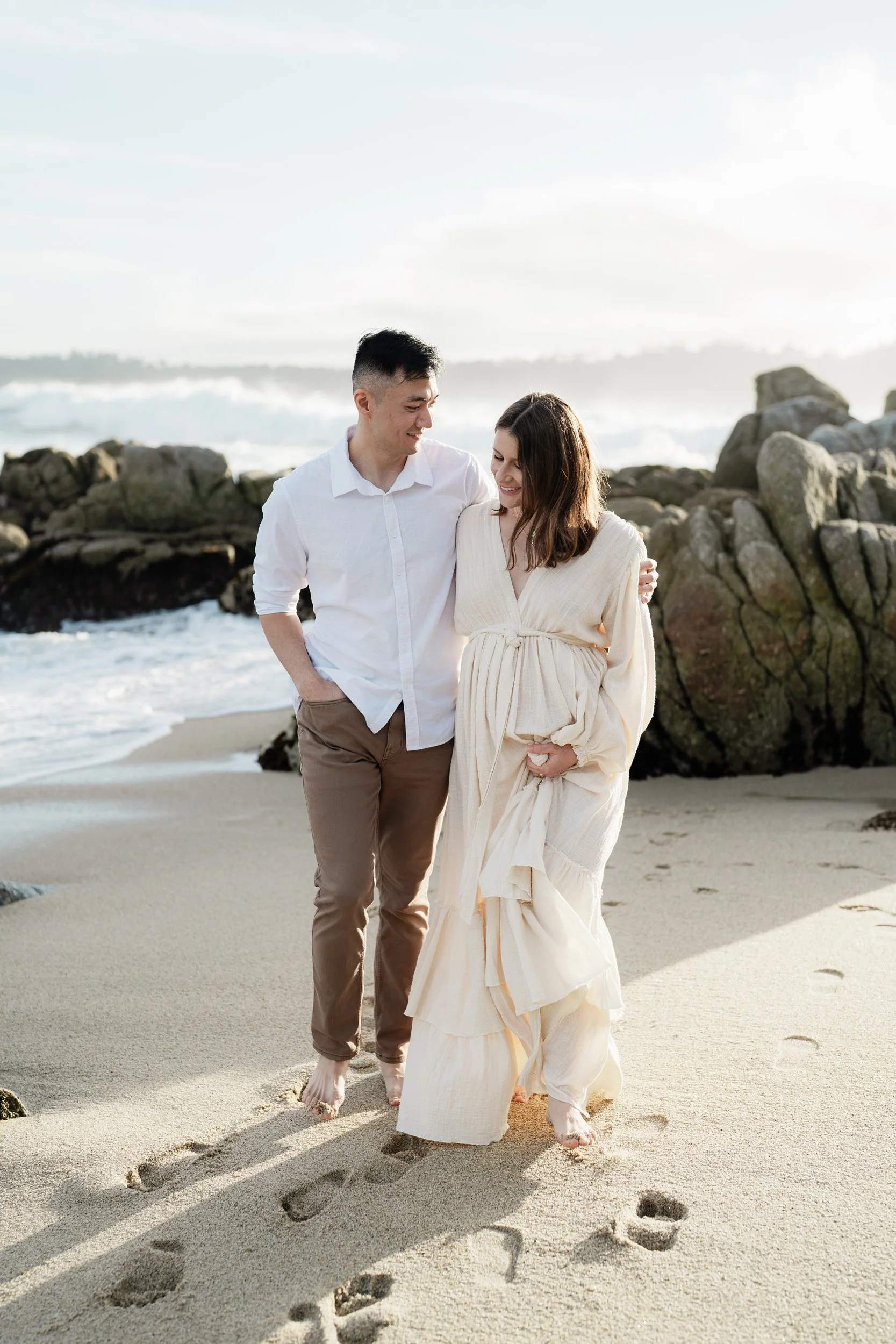 A couple is walking down the beach for their maternity photography in Carmel.