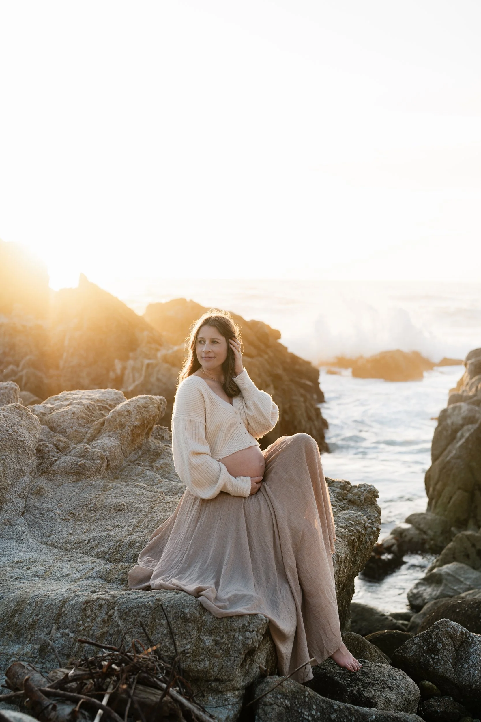 Mom is posing on the rocks at Carmel beach for maternity photos.