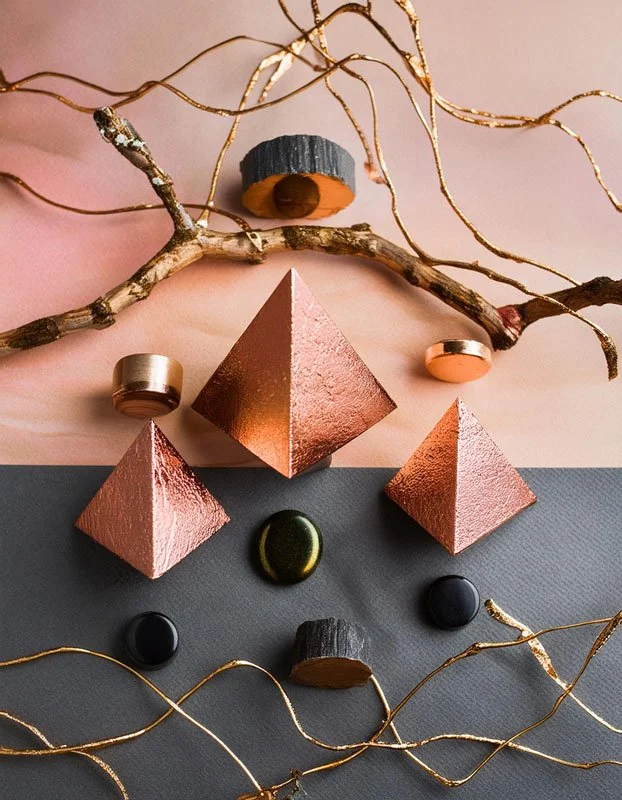 Abstrakte Anordnung aus geometrischen Objekten, Zweigen und Kupferdraht auf geteiltem Hintergrund in Rosa und Grau.