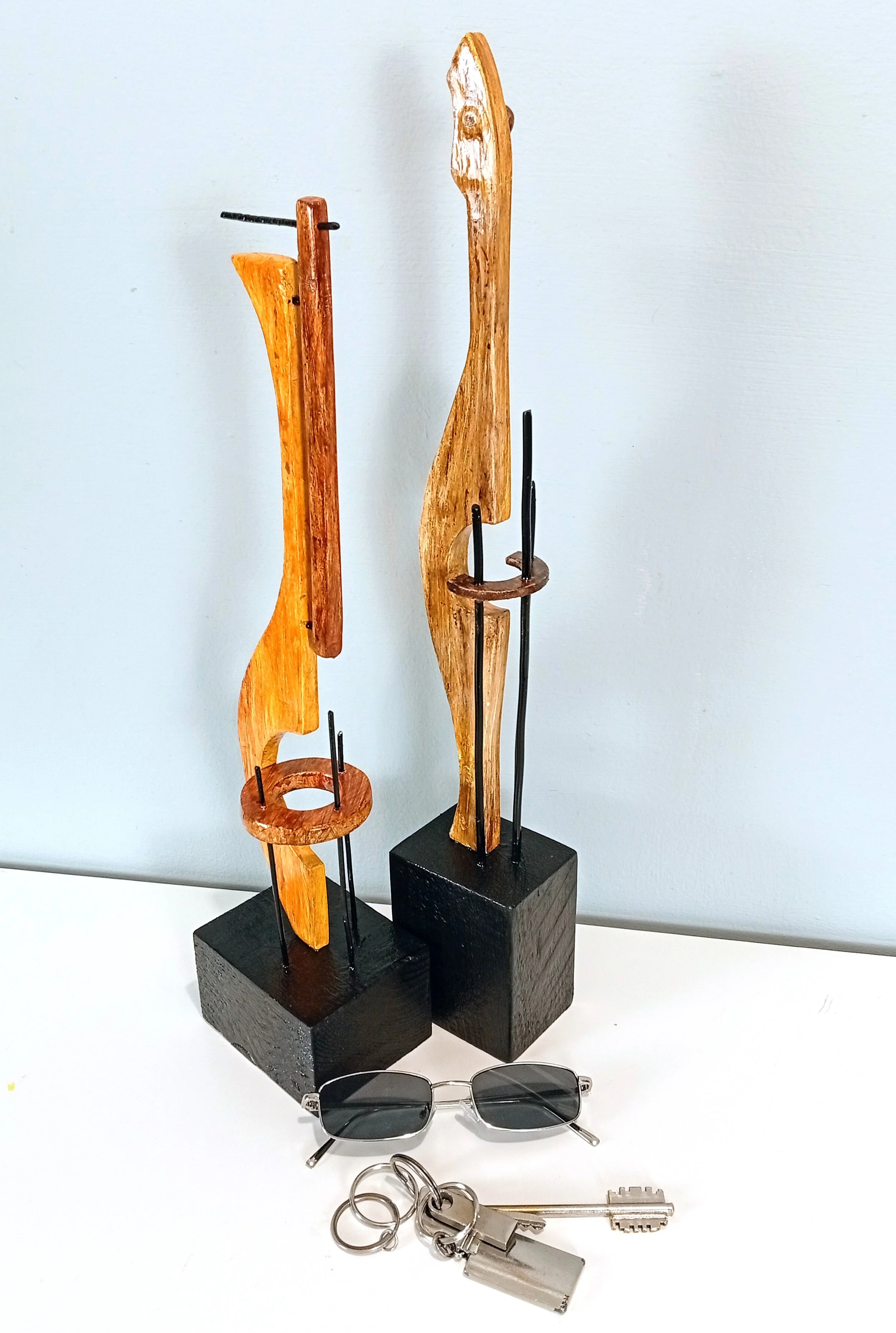 Esculturas abstratas figurativas minimalistas "String Instruments I e II" lado a lado, com base em madeira preta, elementos em arame e massa, acompanhadas por óculos de sol e chaves para escala.