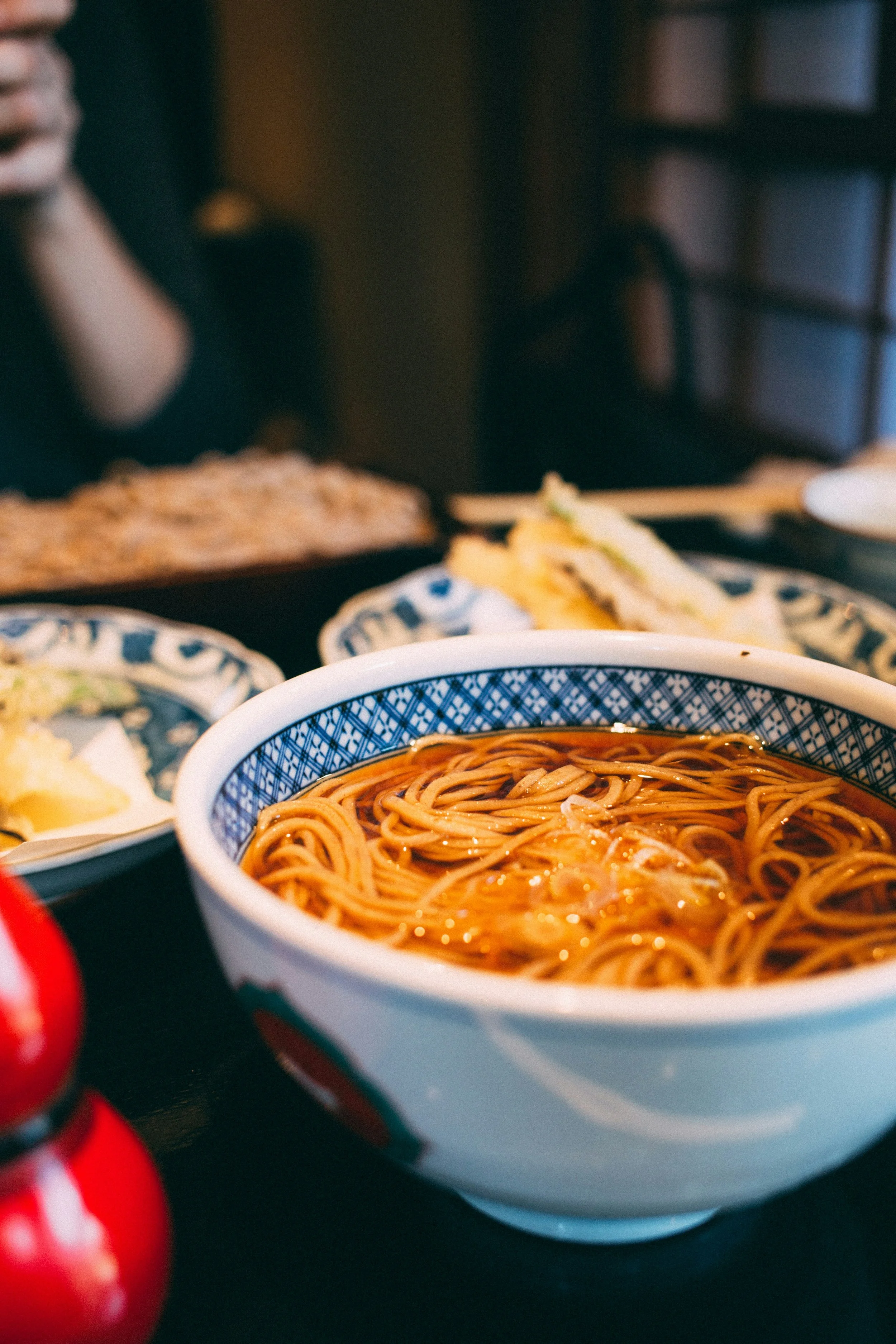 Close-up of a bowl of ramen noodles in broth on a dining table with other dishes in the background