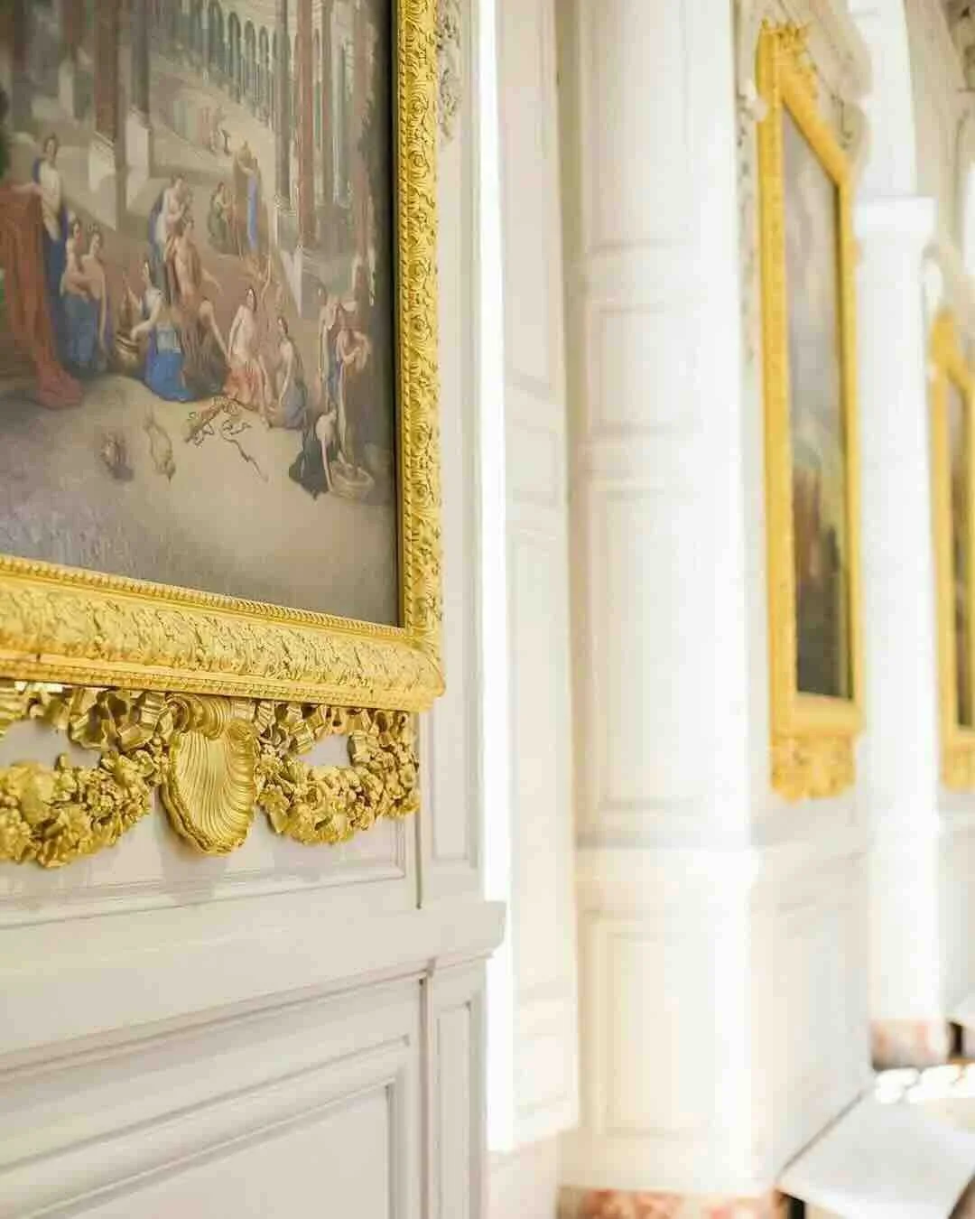 Ornate gold-framed painting hanging on a white wall in a bright, elegant room.