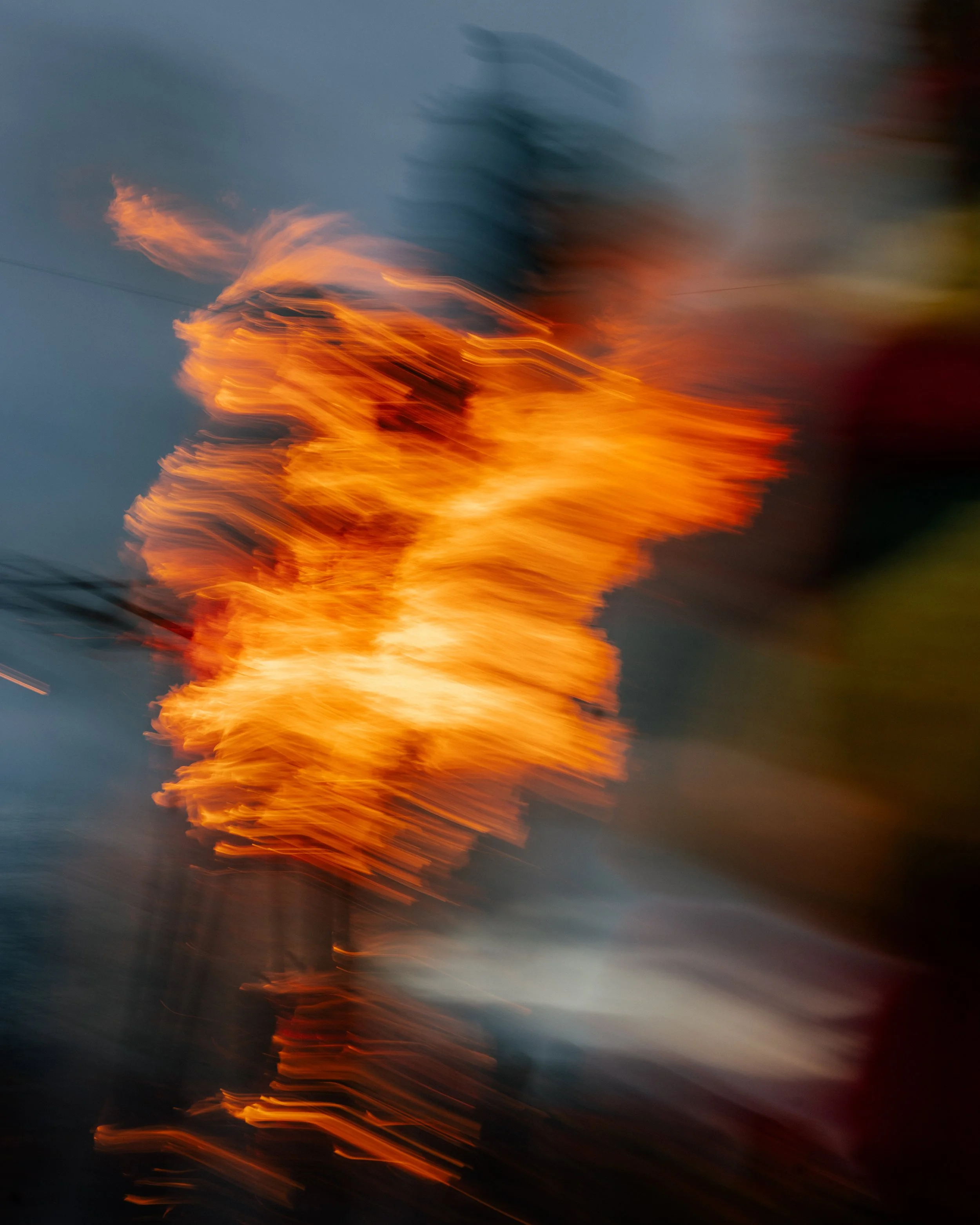 Abstract photo of a large fire at sunset with flames and smoke against a darkening sky.
