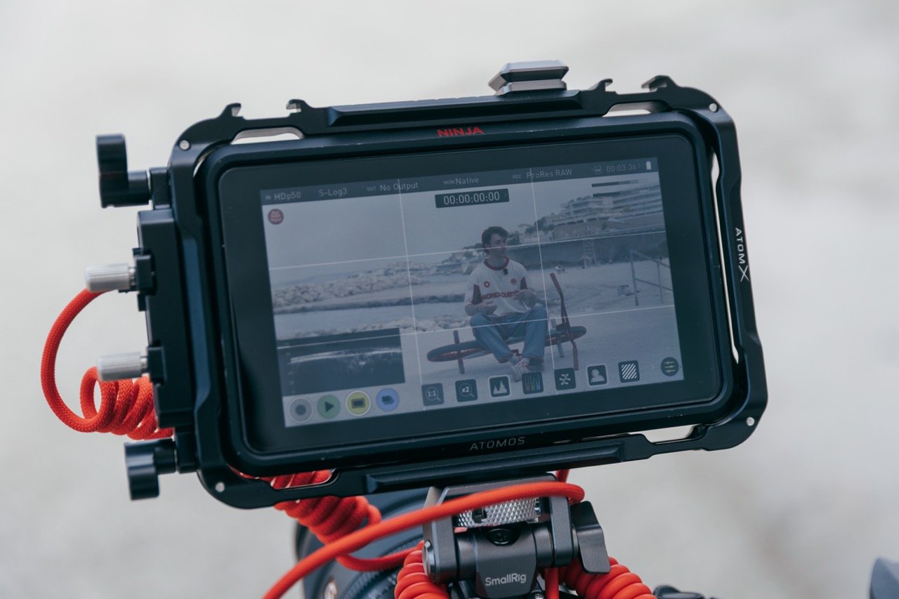 Une caméra enregistreur vidéo avec un écran montrant une personne assise sur un vélo stationnaire à l'extérieur, près de la plage.