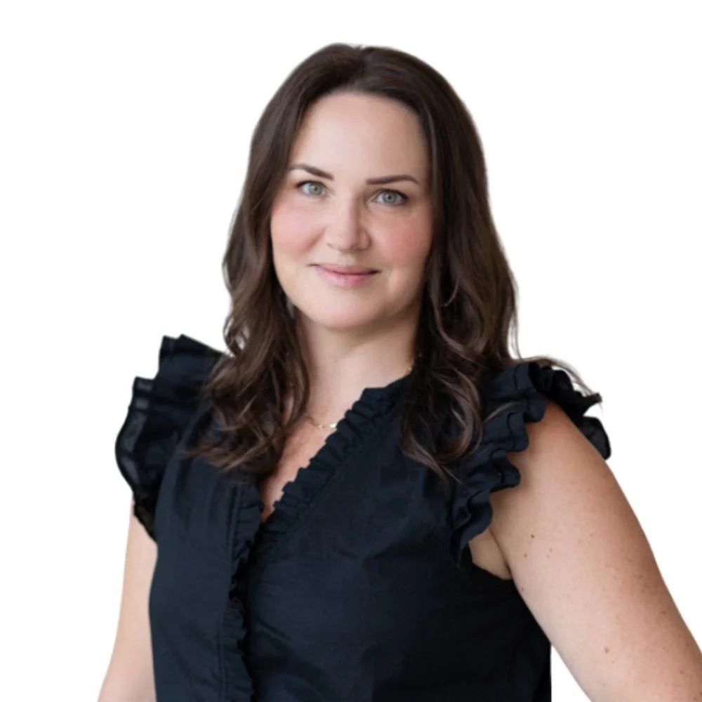 A woman with shoulder-length brown hair and blue eyes, wearing a black sleeveless top with ruffled sleeves, smiling against a white background.