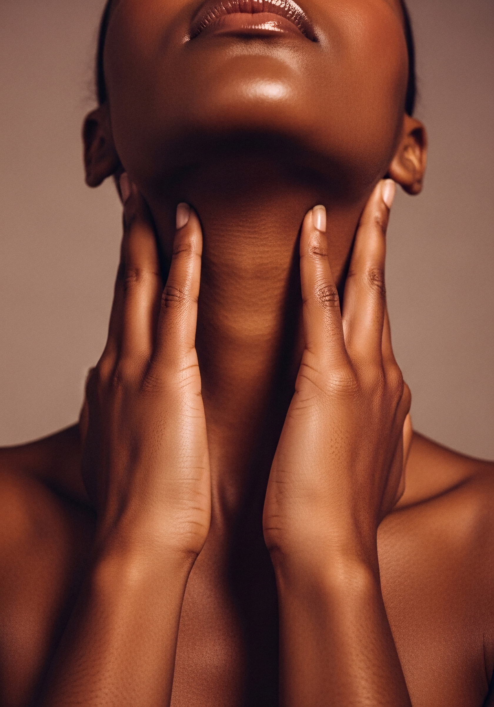 A close-up of a person's face and neck with hands touching their neck, showcasing smooth, brown skin and glossy lips. surgery, intervention, surgical, recovery, face lift, tightening, firming, collagen
