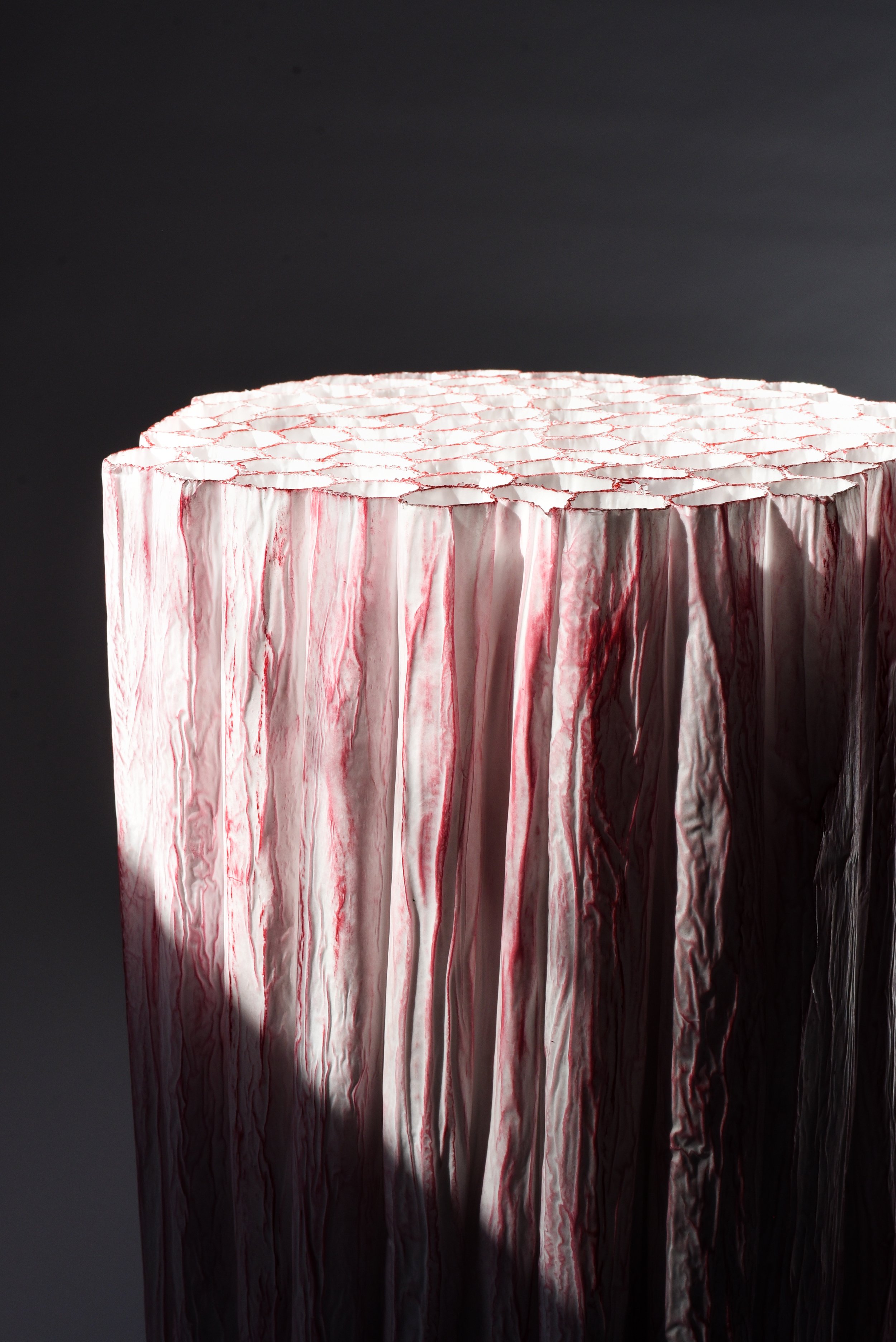 A close-up of a textured, vertical white and pink patterned sculpture with a dark background.