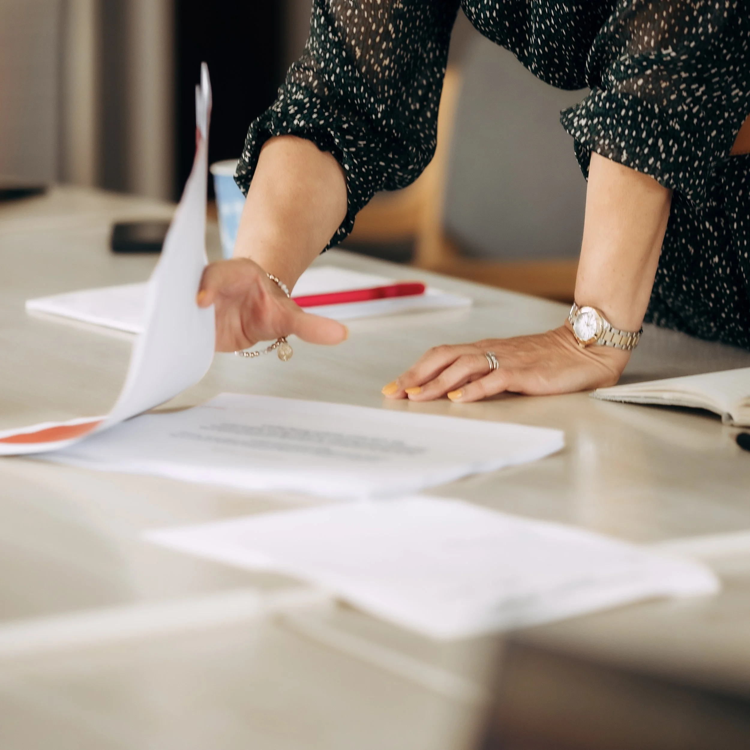 People working at a desk with papers, documents, and writing utensils.