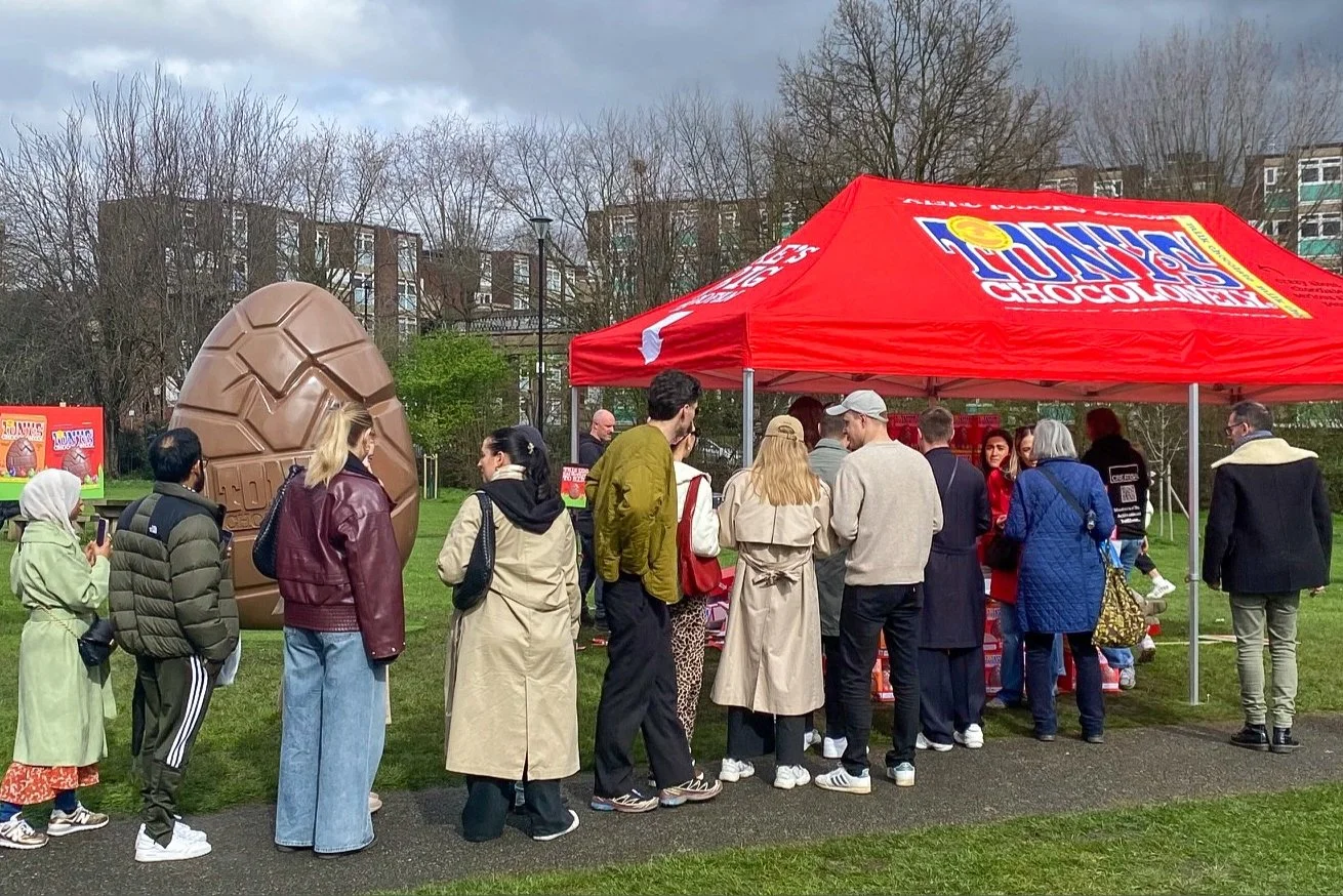People queuing at a Tony's Chocolonely stand, with a giant chocolate Easter egg in the background.