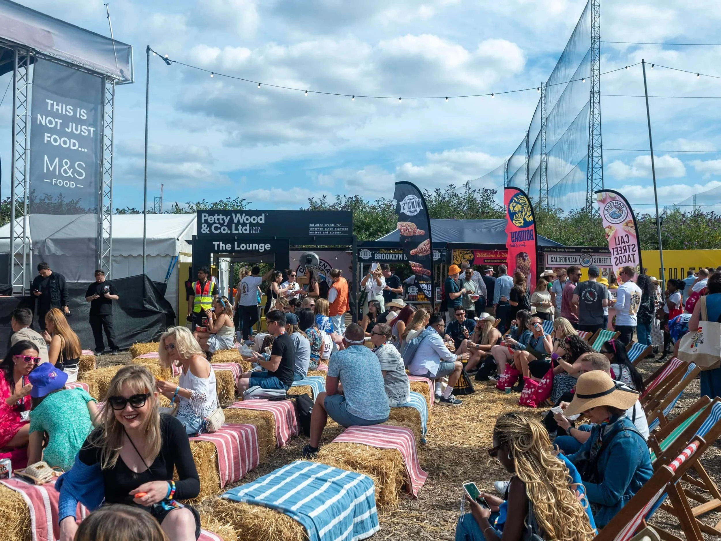Crowd of people seated on hay bales and deck chairs at Barcode Festival with Urban Food Brands multi-brand event activation in the background.