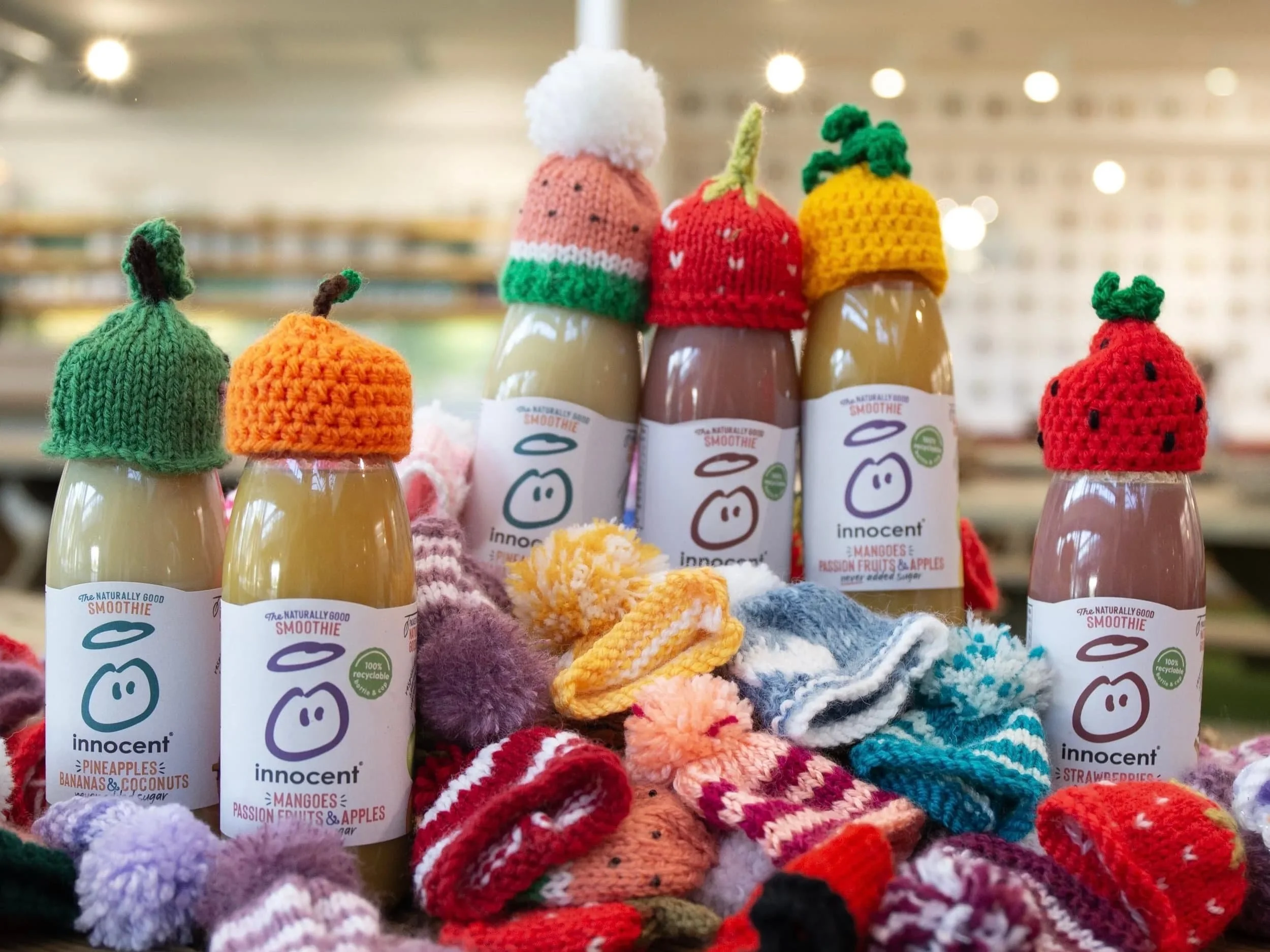 Bottles of Innocent smoothies with knitted hats resembling fruits and berries, surrounded by lots more knitted hats.