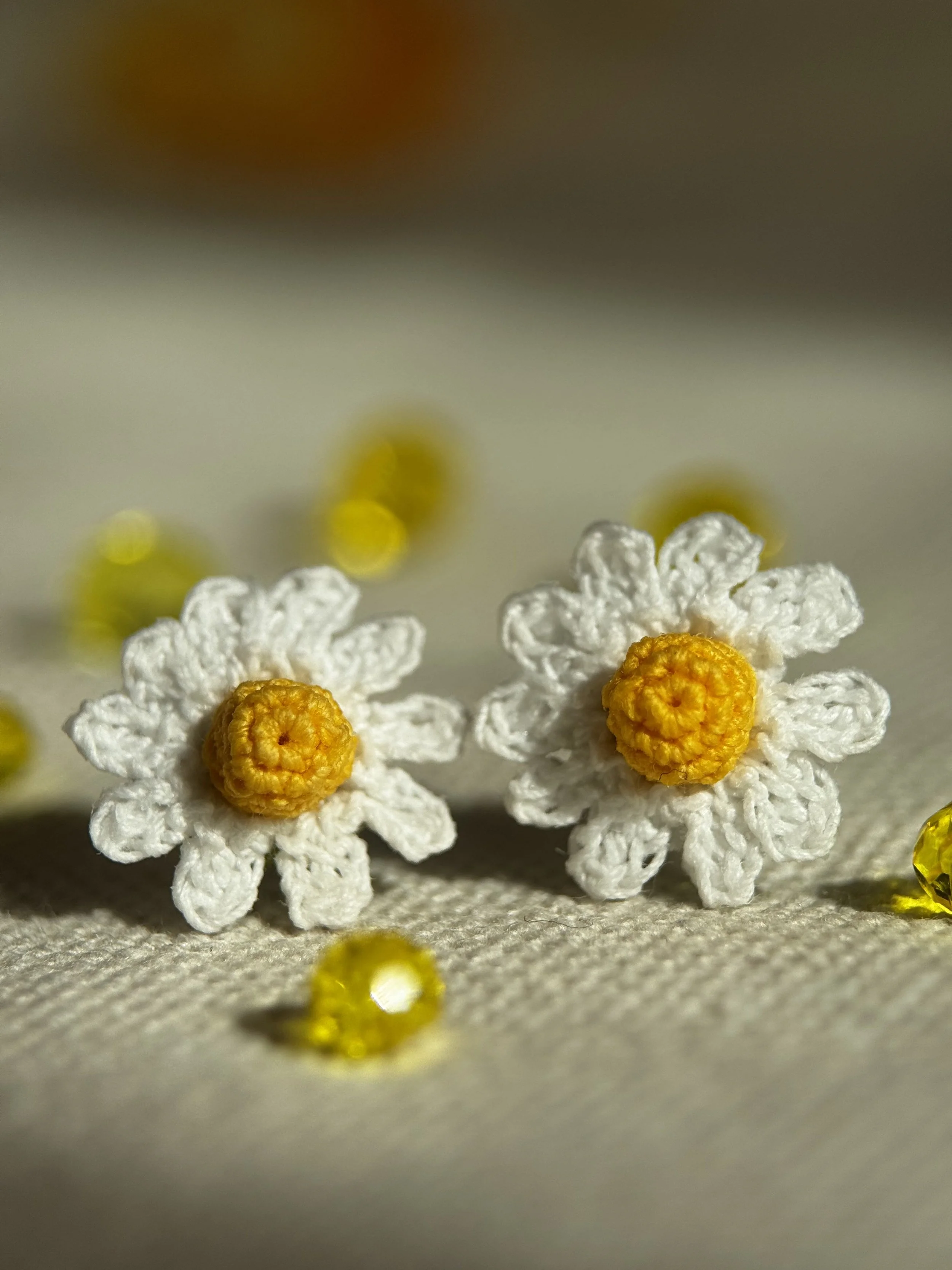 Fiori di tessuto fatti a mano con petali bianchi e centri gialli, decorati con piccole palline gialle su uno sfondo con luci gialle.