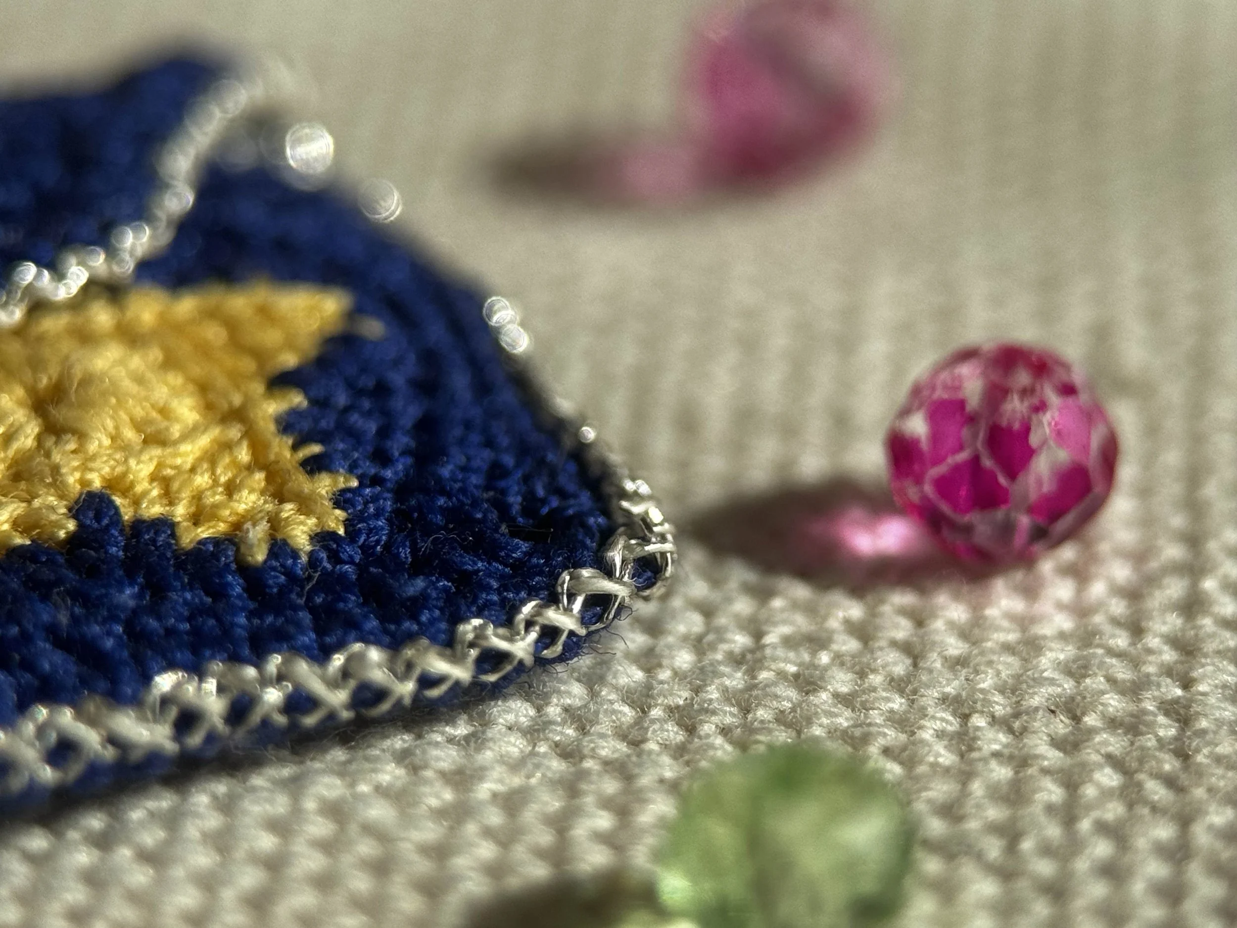 Prima di tutto c'è una foto ravvicinata di un orsetto di peluche blu e giallo con dettagli in pizzo, accompagnato da due bacche rosa decorativi, il tutto su una superficie di tessuto beige.