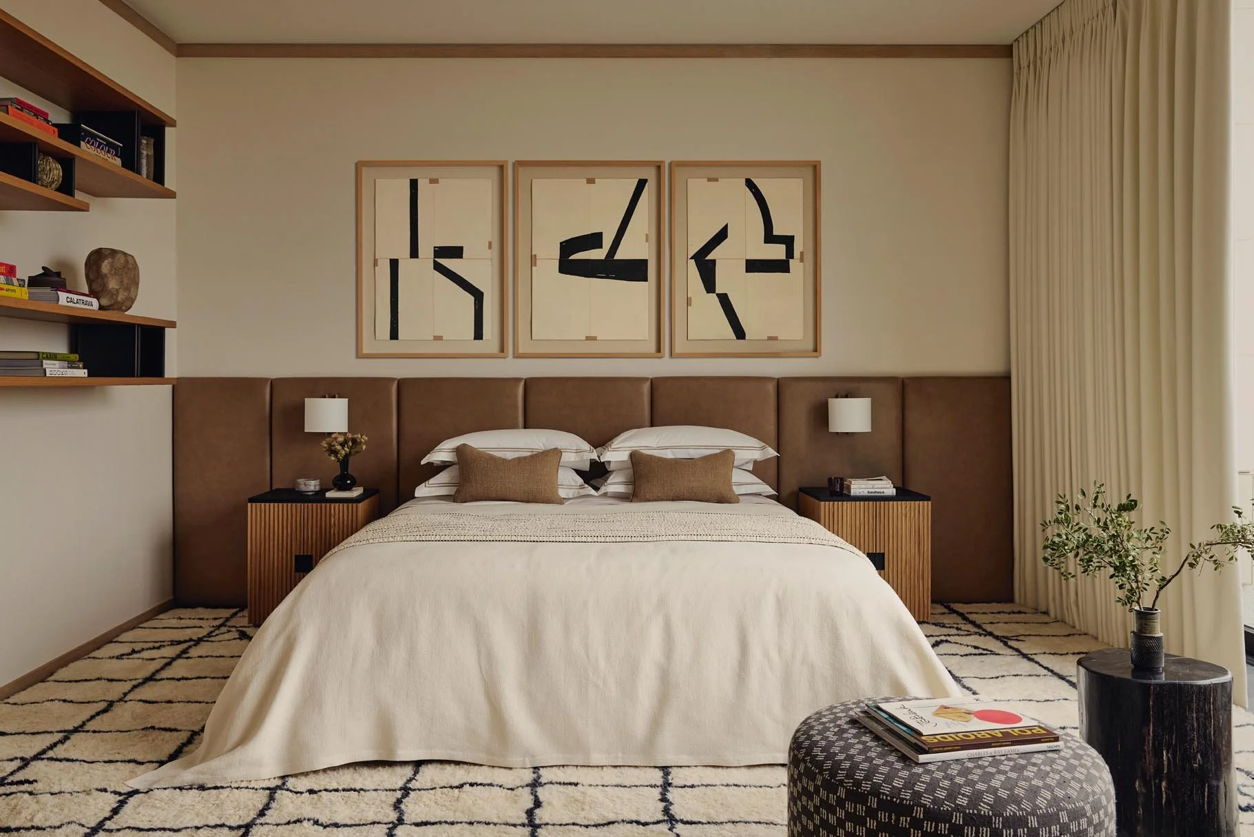 A modern and stylish bedroom at The Peninsula Hotel Residences featuring a bed, framed abstract art, curated bookshelves, a side table with floral décor, and a plant by the window, combining sophisticated design and serene comfort.