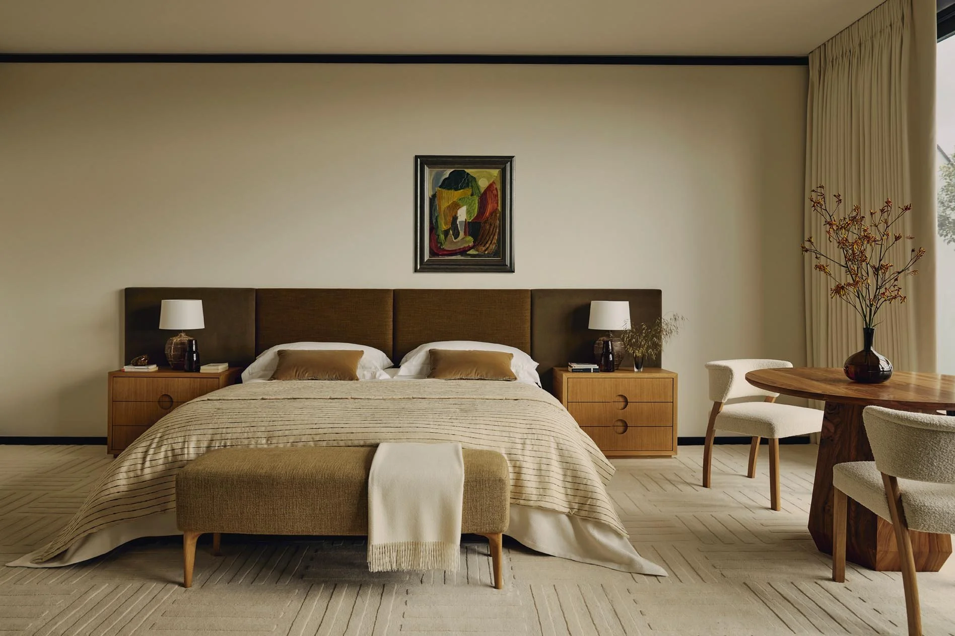 A luxury bedroom with a bed, painting above the headboard, bedside lamps, wooden nightstands, a round wooden table with chairs, bespoke rug, and a large window with curtains, exuding a calm, inviting atmosphere at The Peninsula Hotel Residences